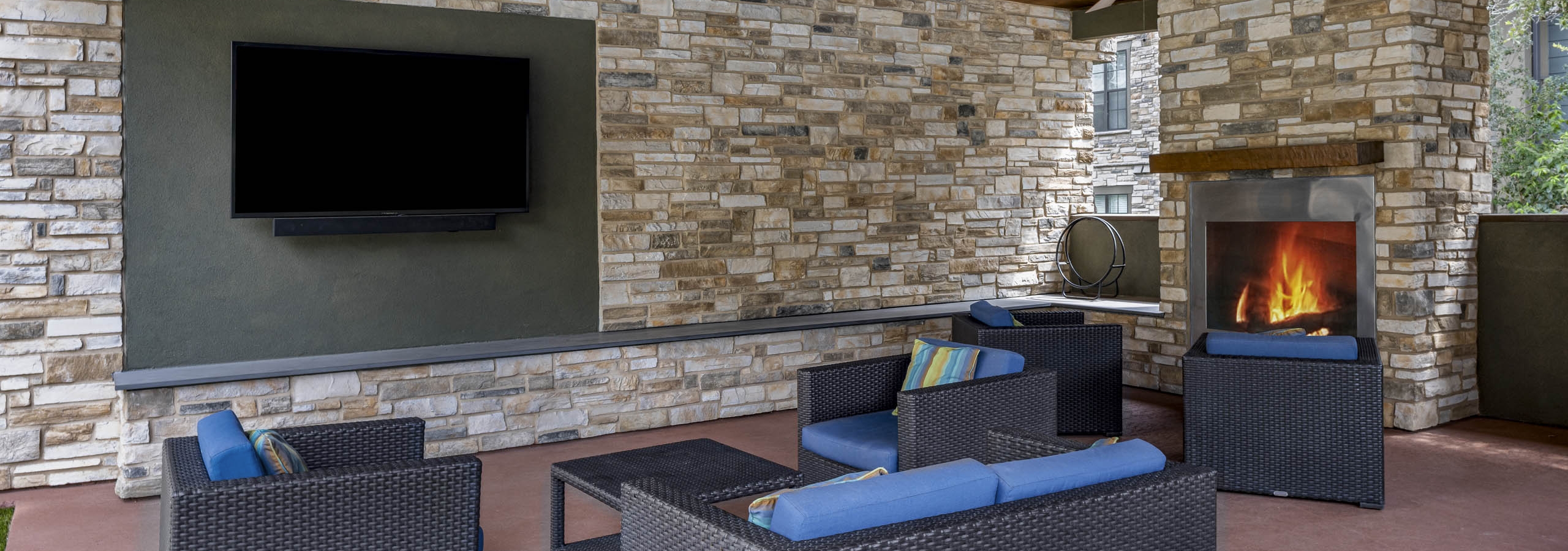 AMLI Covered Bridge cabana with brown wicker seating and blue cushions surrounded by stacked stone walls and fireplace and TV