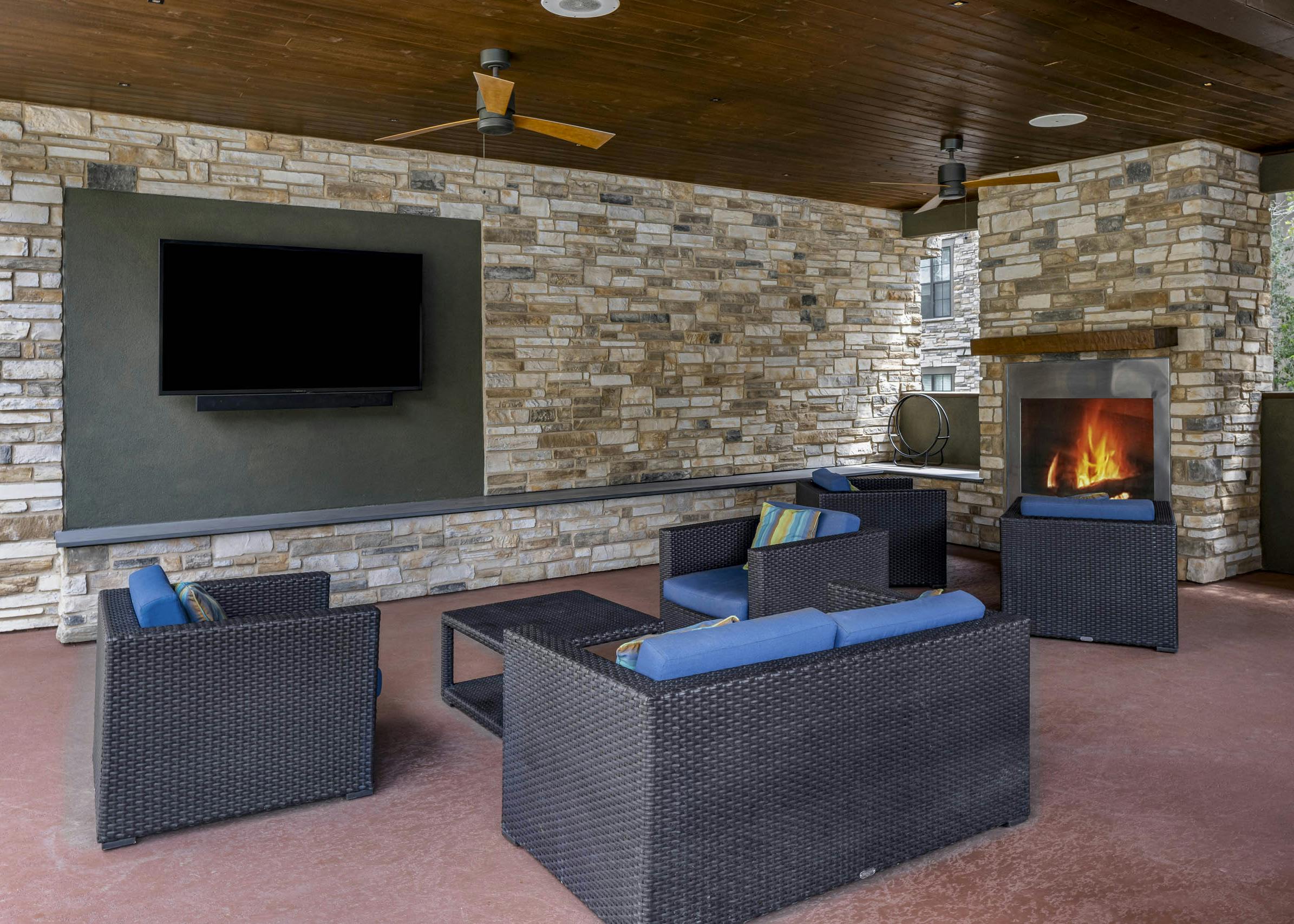 AMLI Covered Bridge cabana with brown wicker seating and blue cushions surrounded by stacked stone walls and fireplace and TV