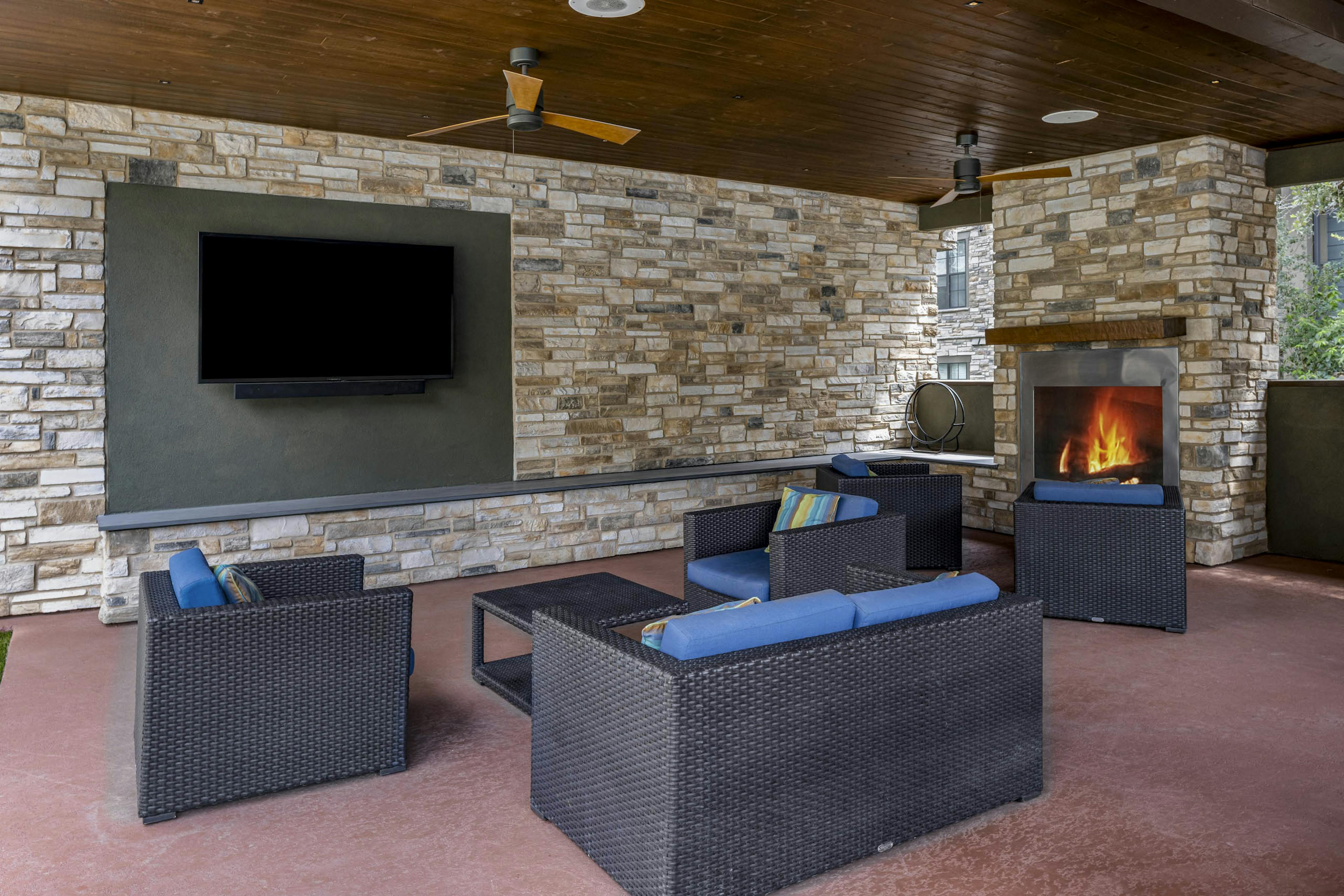 AMLI Covered Bridge cabana with brown wicker seating and blue cushions surrounded by stacked stone walls and fireplace and TV