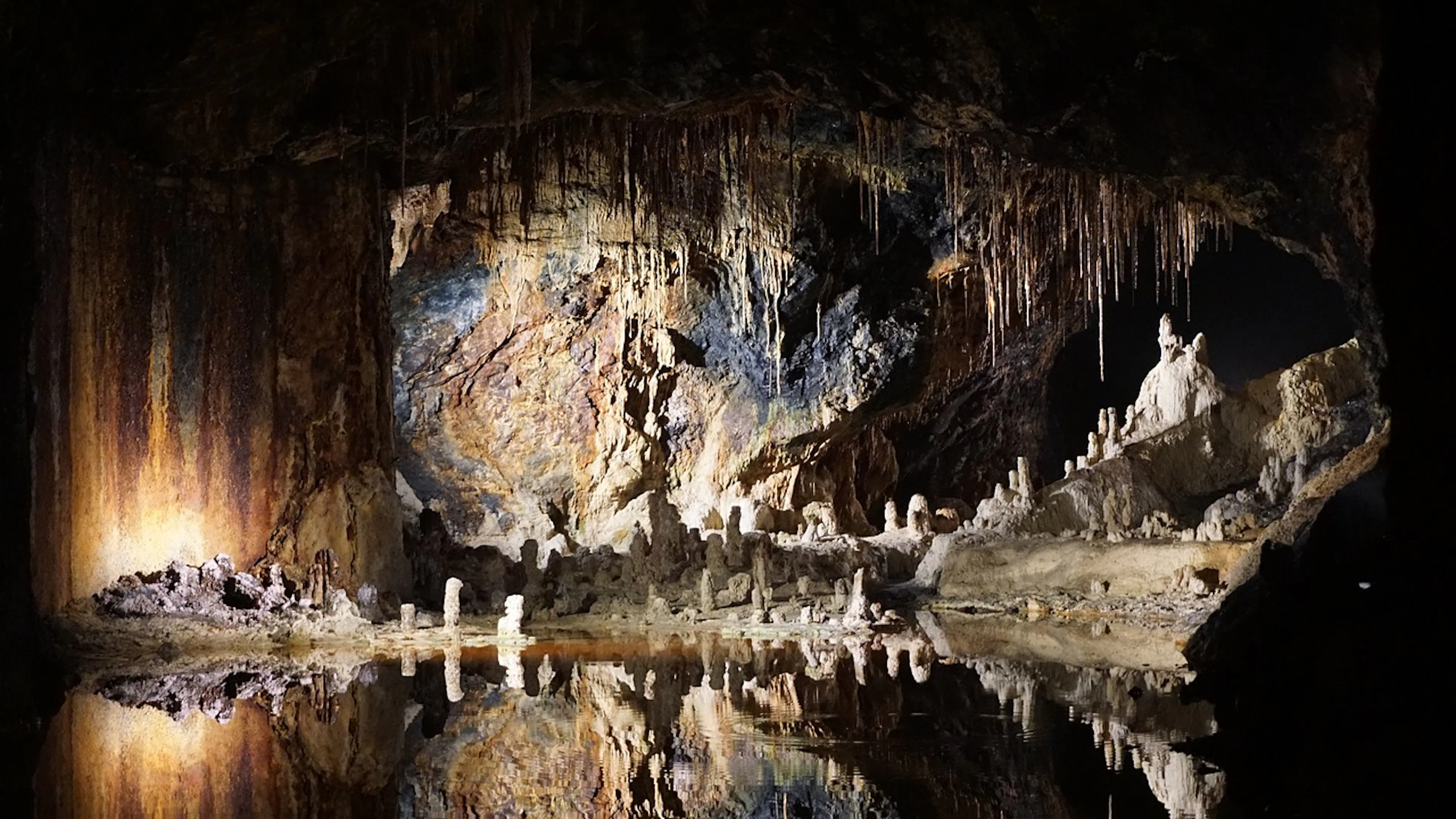 An underground lake reflecting a cave ceiling full of stalactites and pillars