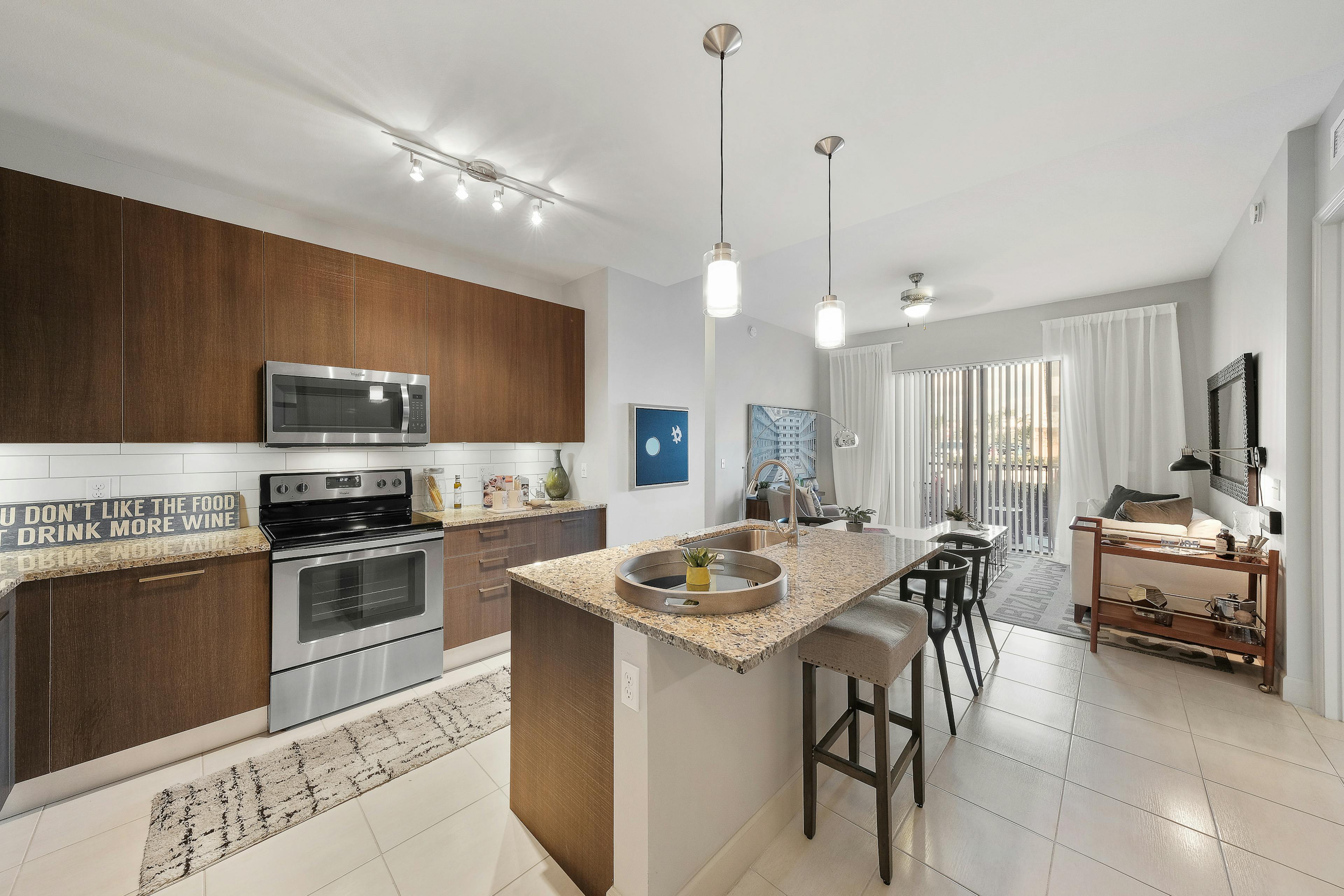 AMLI 8800 apartment with island kitchen with stools, stainless steel appliances, wood cabinetry and peek into living area 