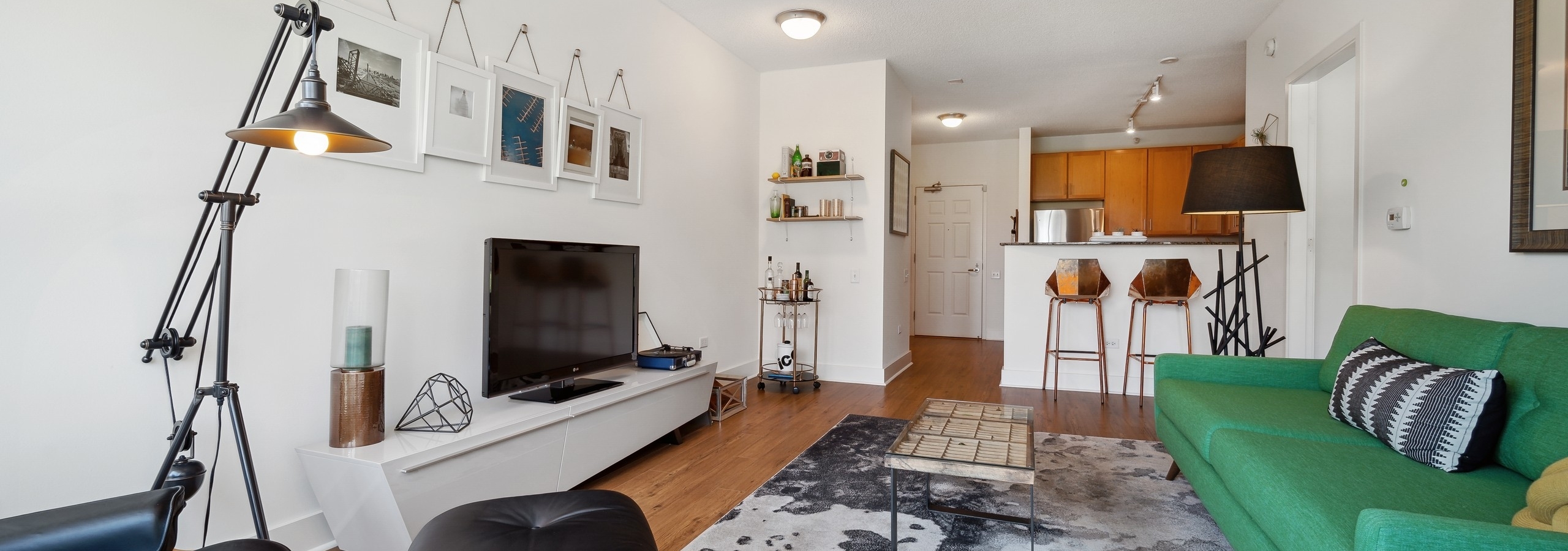 AMLI 900 apartment living room with wood flooring and view to a kitchen with granite countertops and bar stools