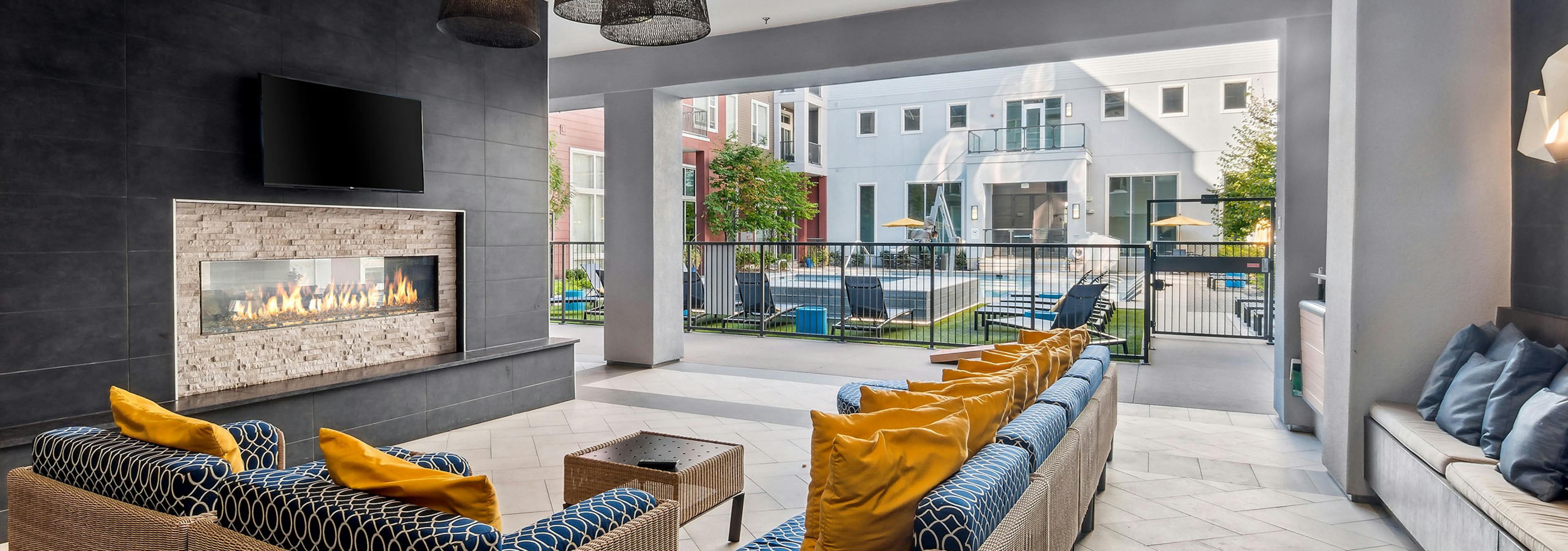 Outdoor living room with couches with big yellow pillows and fireplace and TV at AMLI Denargo Market with view of the pool