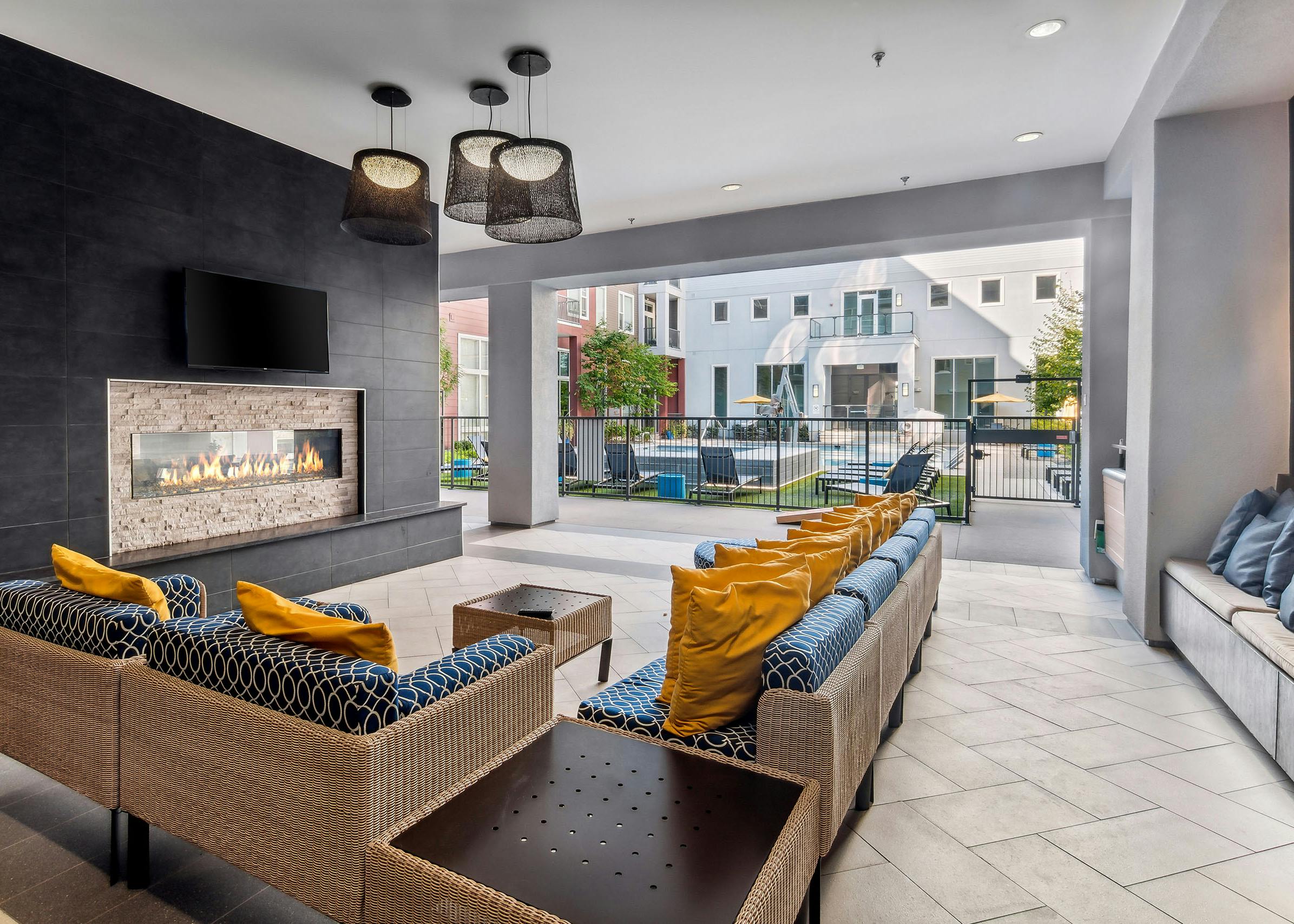 Outdoor living room with couches with big yellow pillows and fireplace and TV at AMLI Denargo Market with view of the pool