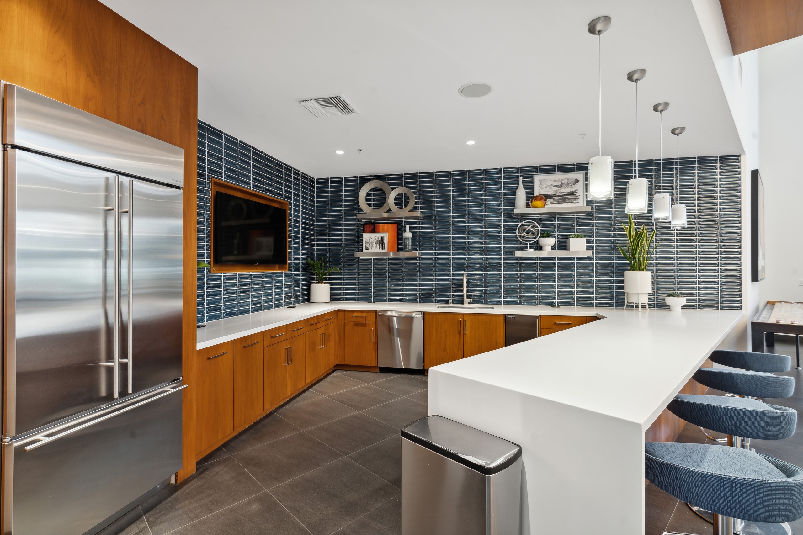 Clubroom kitchen with stainless steel appliances and  blue tile backsplash walls and TV at AMLI Uptown Orange apartments