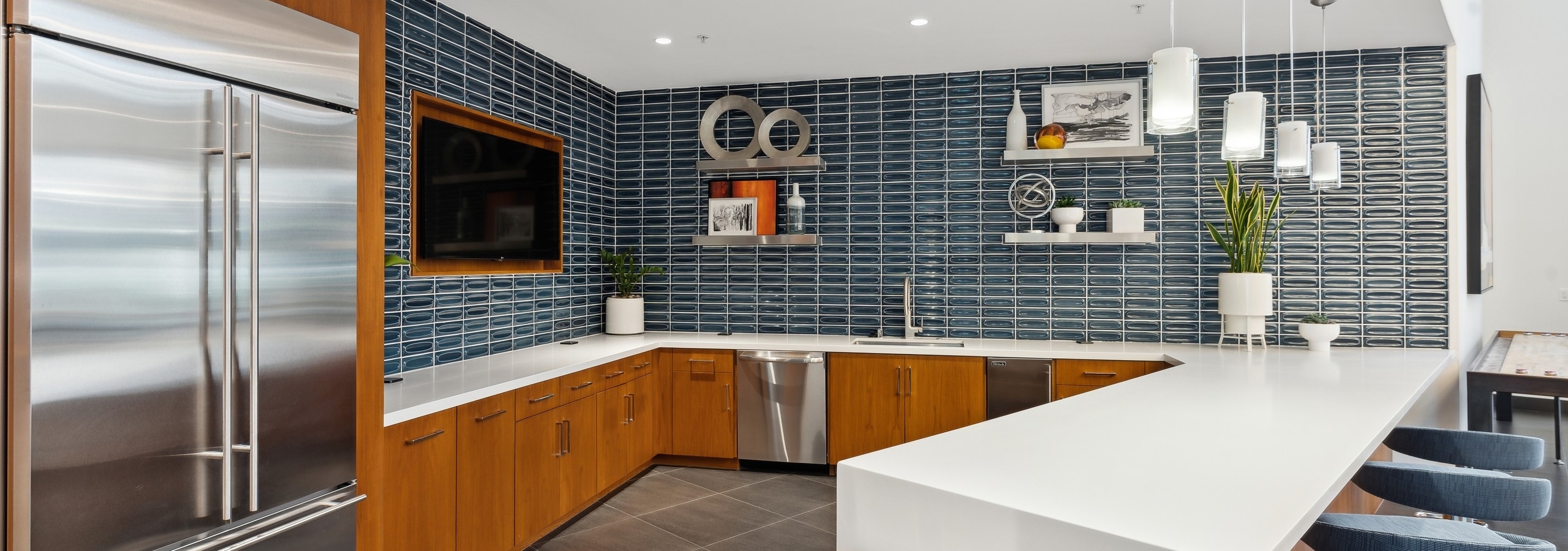 Clubroom kitchen with stainless steel appliances and  blue tile backsplash walls and TV at AMLI Uptown Orange apartments