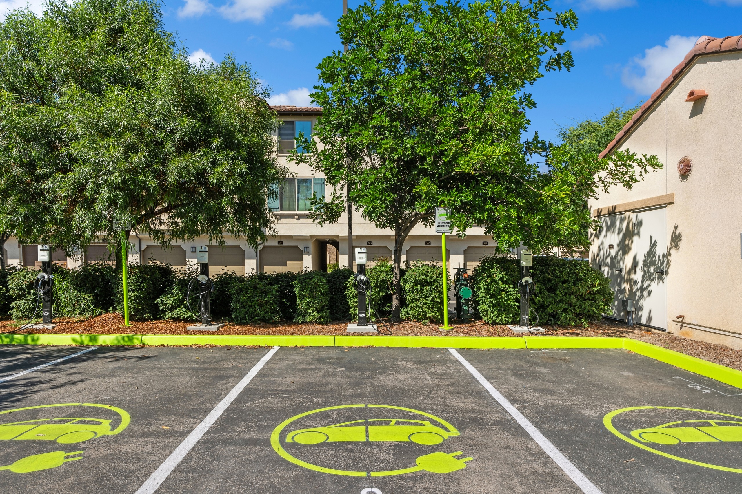 4 dedicated  EV charging station parking spots with neon yellow paint and chargers in front of bushes at AMLI Spanish Hills 