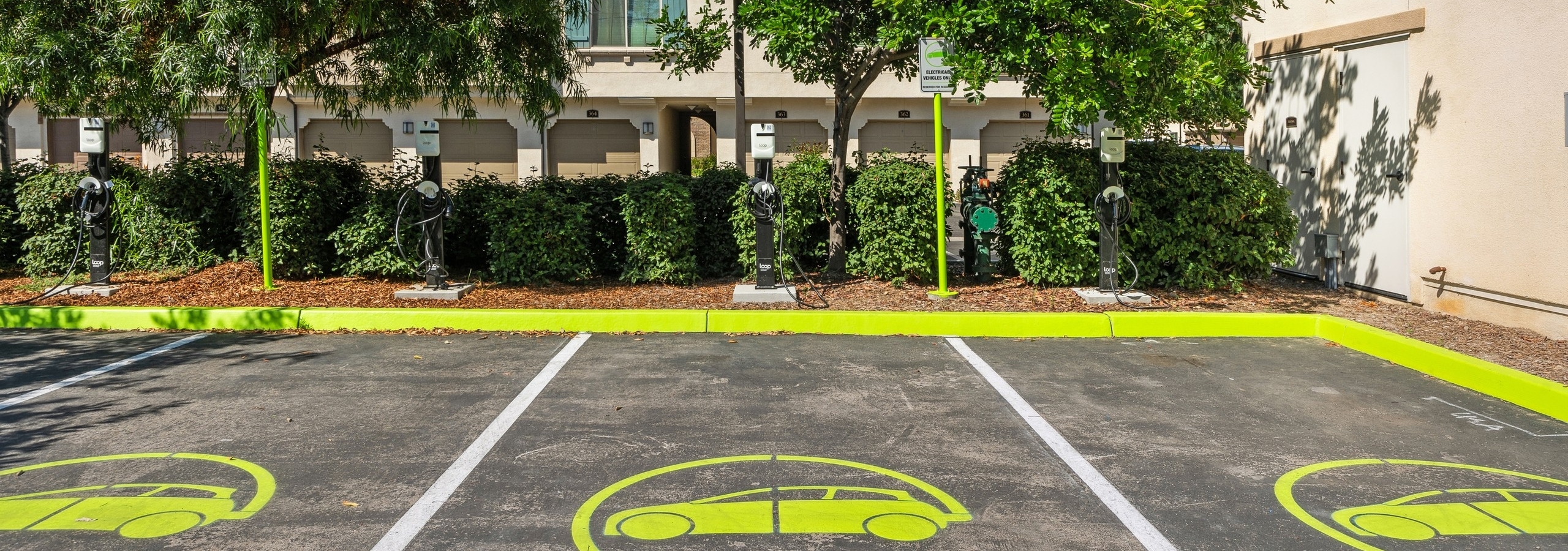4 dedicated  EV charging station parking spots with neon yellow paint and chargers in front of bushes at AMLI Spanish Hills