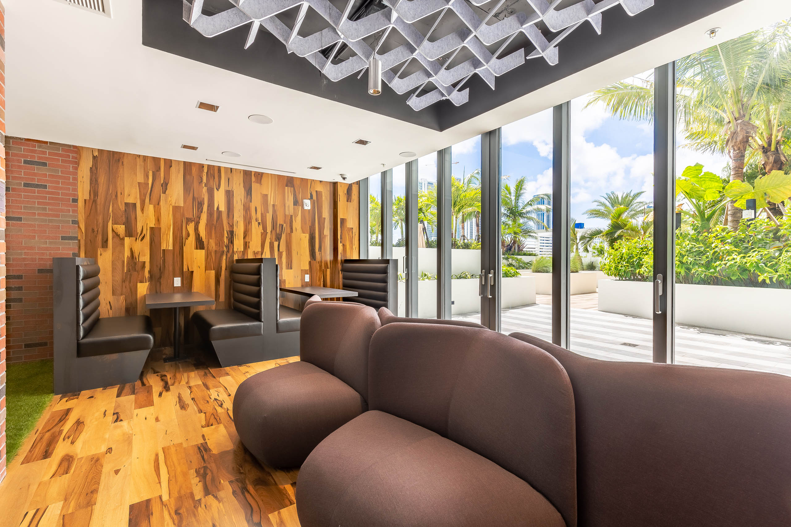 AMLI Midtown Miami apartments saloon with wood panel floor and walls and modern sofa and booth seating with glass patio doors