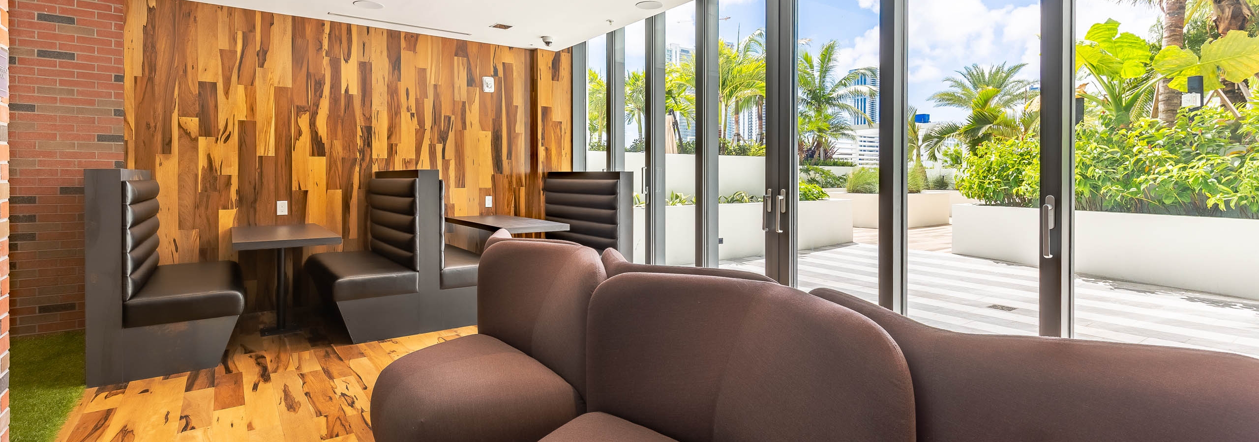AMLI Midtown Miami apartments saloon with wood panel floor and walls and modern sofa and booth seating with glass patio doors