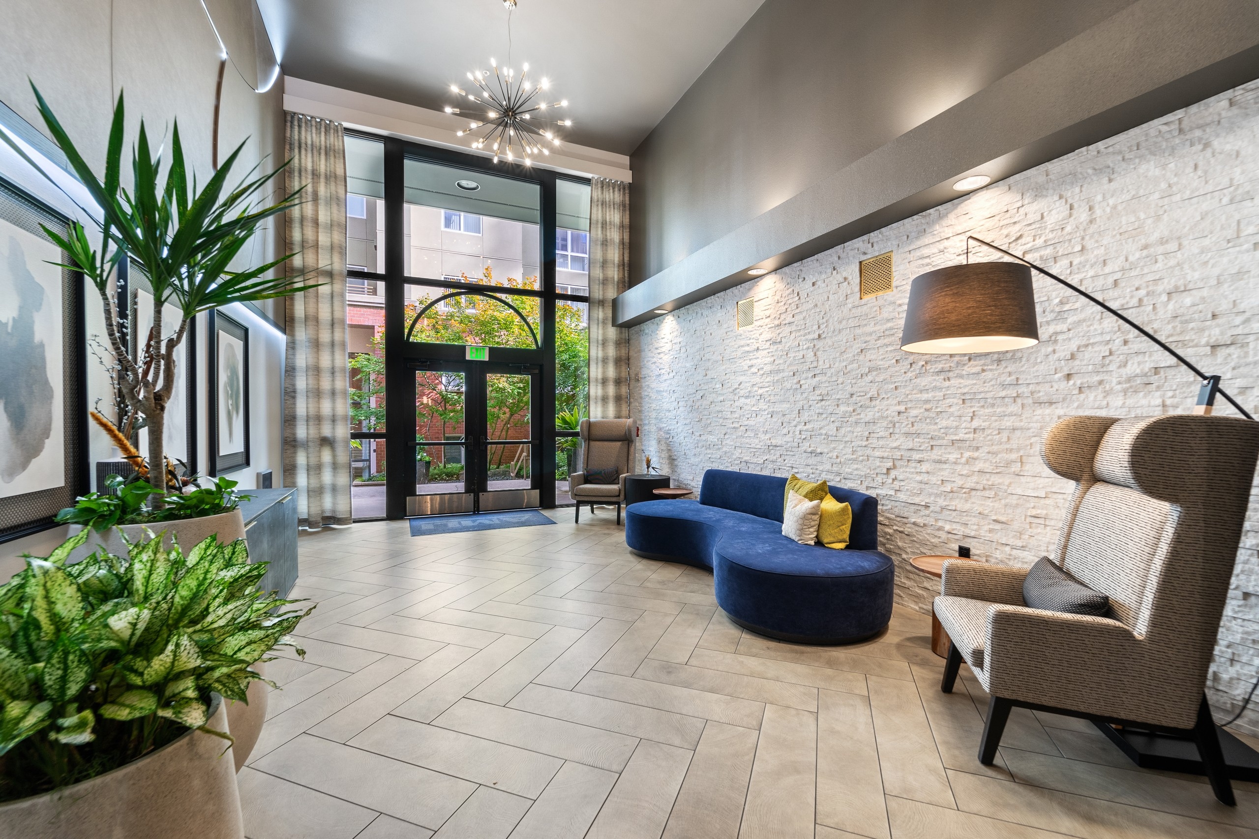 Lobby at AMLI Bellevue Park apartments with two story window and door and blue couch and 2 chairs and plants on opposite wall