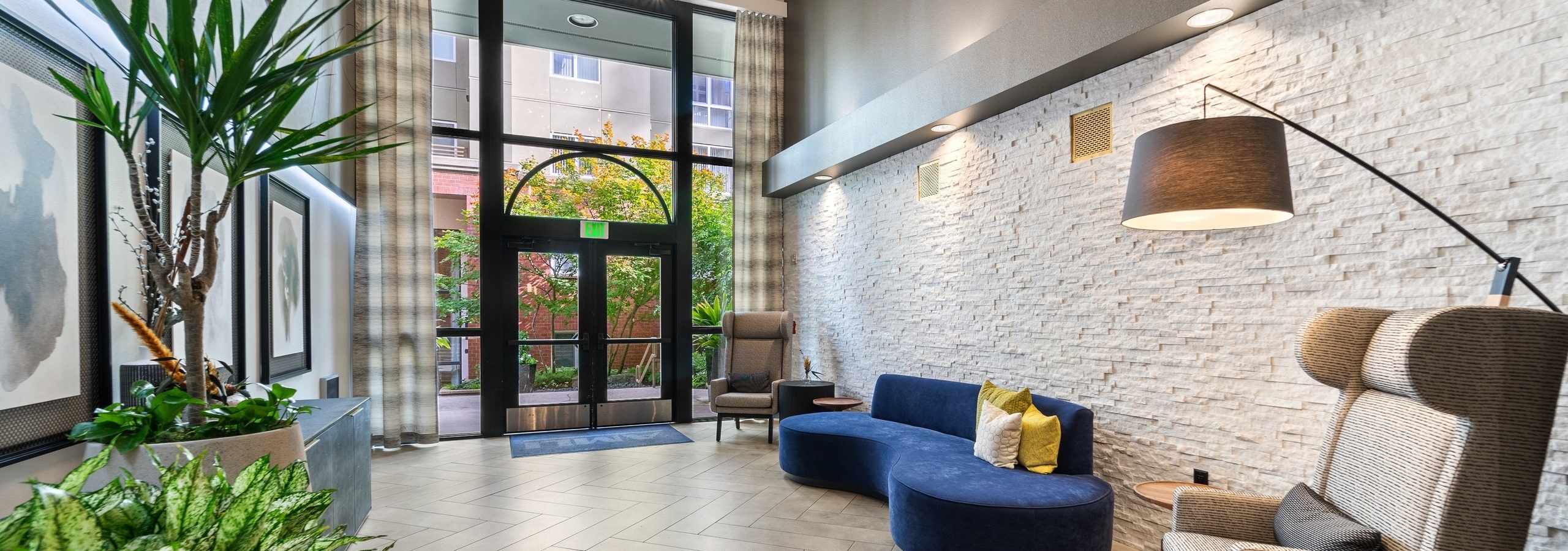 Lobby at AMLI Bellevue Park apartments with two story window and door and blue couch and 2 chairs and plants on opposite wall