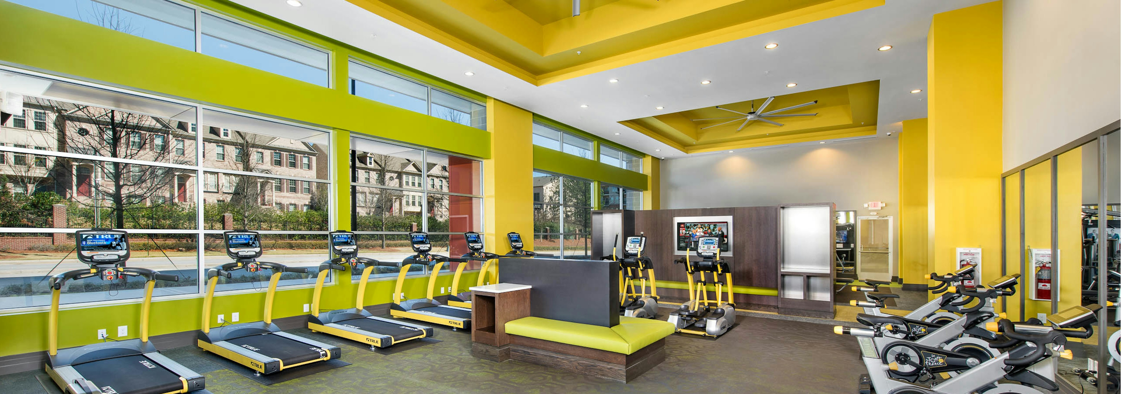 Interior of fitness center at AMLI Buckhead with vibrant yellow walls and large windows in front of a line of treadmills