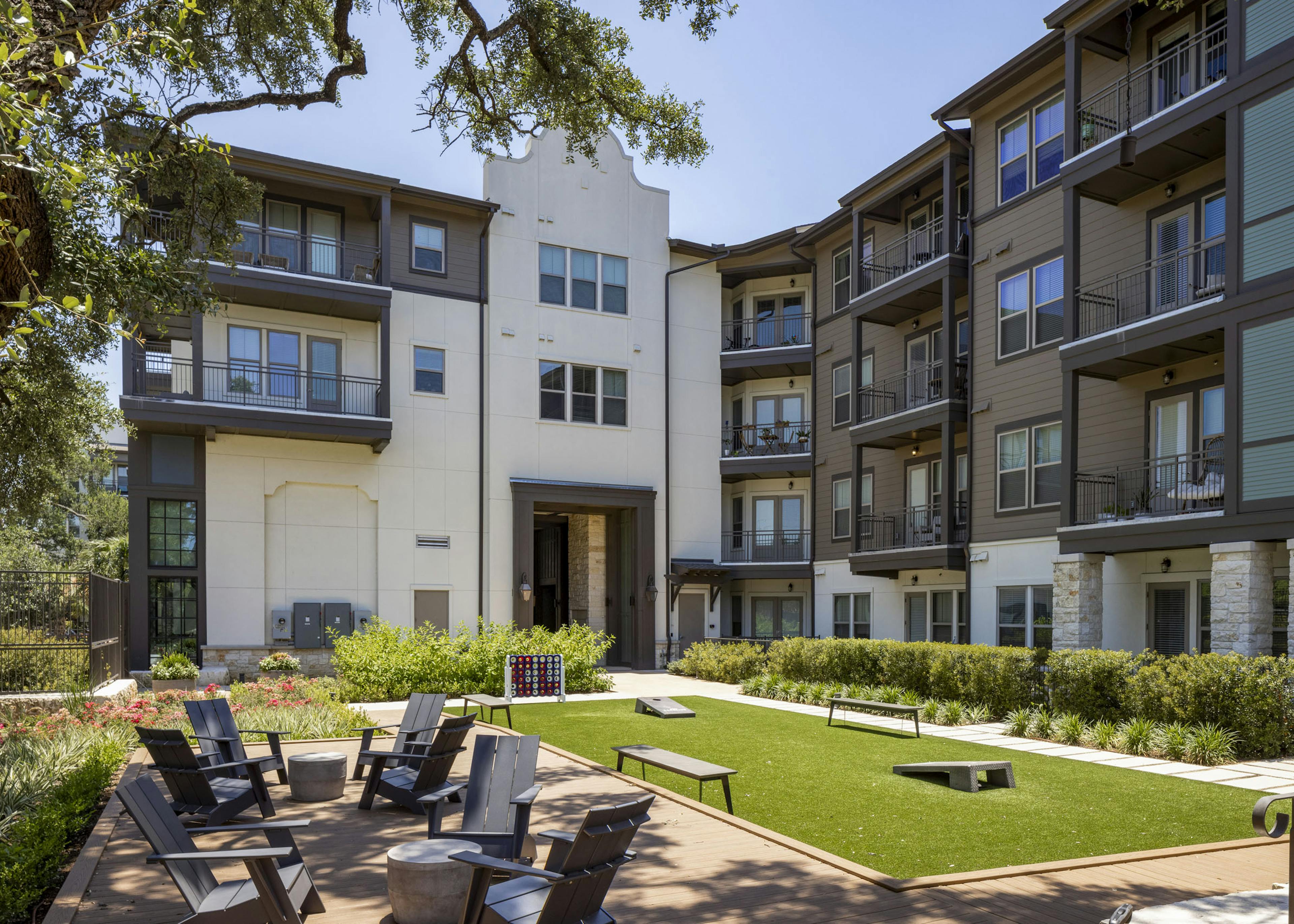 Daytime view of AMLI Lakeline bocce ball court with various outdoor games on  green turf  next to shaded outdoor seating area
