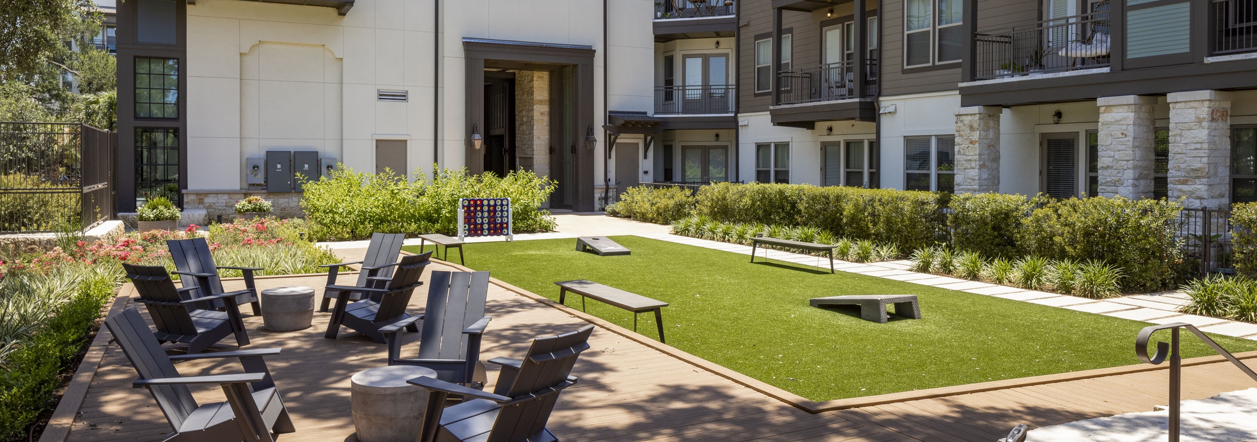 Daytime view of AMLI Lakeline bocce ball court with various outdoor games on  green turf  next to shaded outdoor seating area