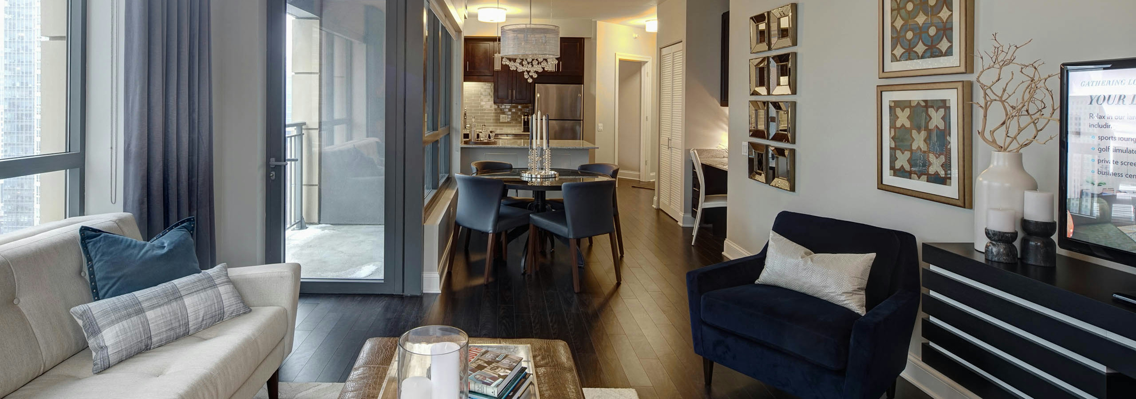 View of living room at AMLI River North with neutral decor and dark wood floors connecting to the kitchen in the back ground