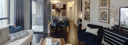 View of living room at AMLI River North with neutral decor and dark wood floors connecting to the kitchen in the back ground