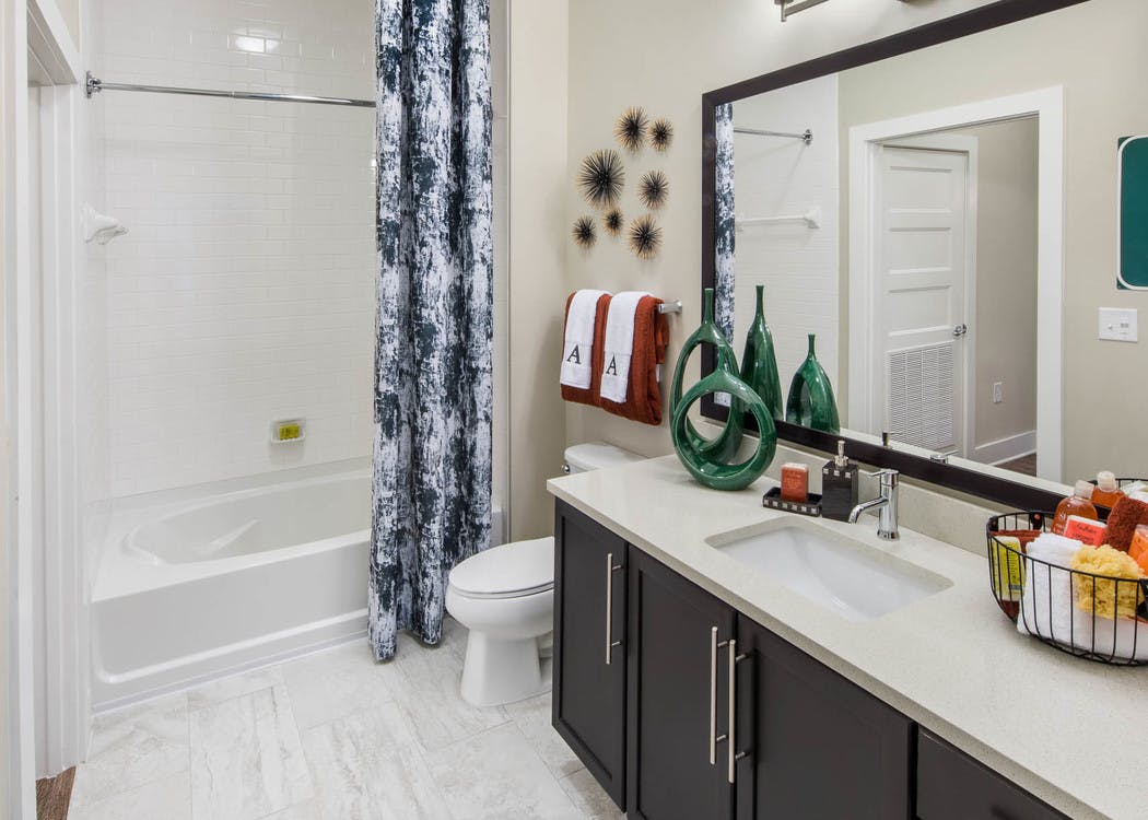Bathroom at AMLI Buckhead with dark wood vanity sink and a white bathtub with a dark grey and white patterned curtain