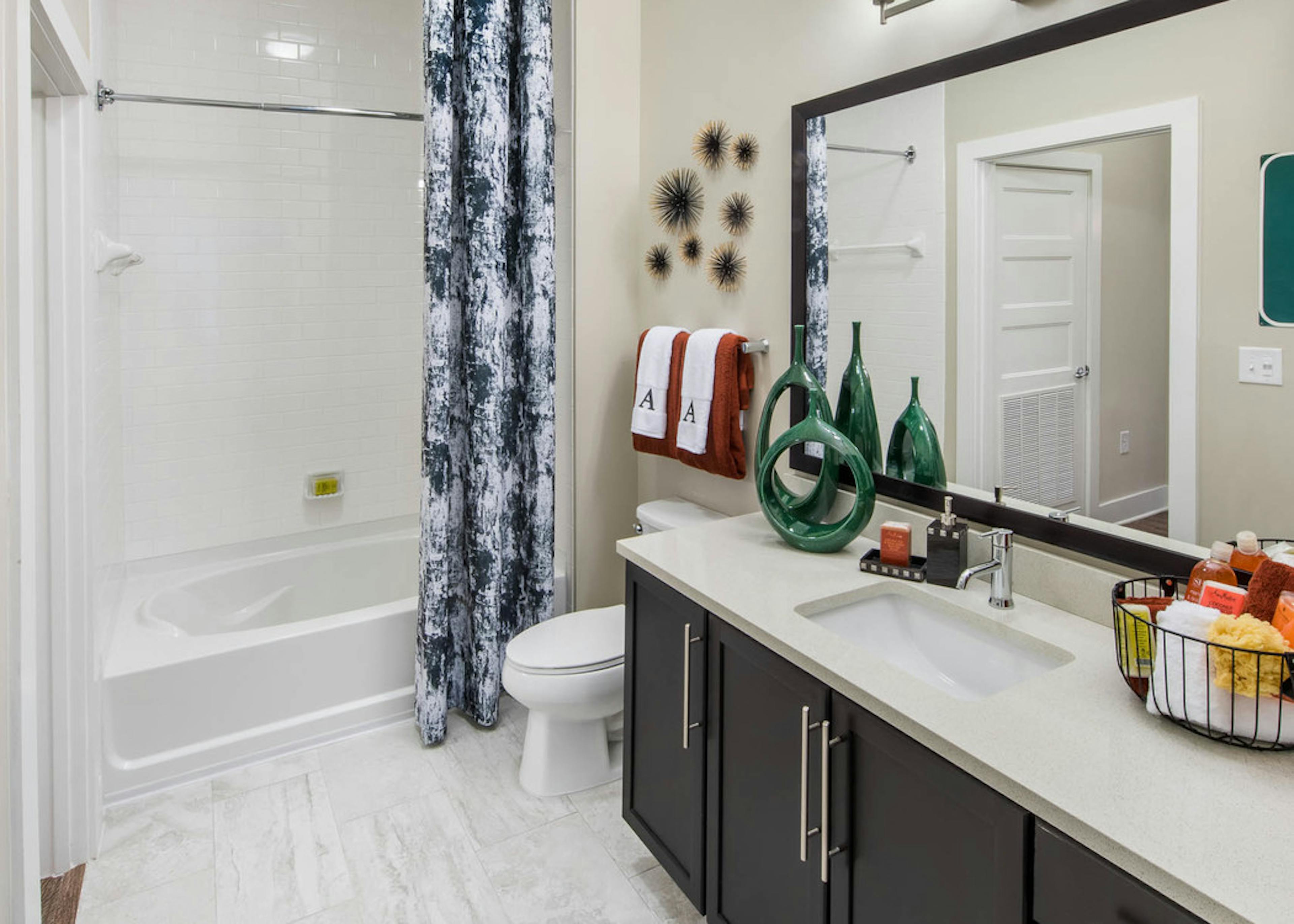 Bathroom at AMLI Buckhead with dark wood vanity sink and a white bathtub with a dark grey and white patterned curtain