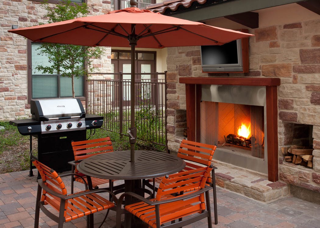 Daytime view of AMLI at Escena brick outdoor fireplace with brown table and four orange chairs and grill