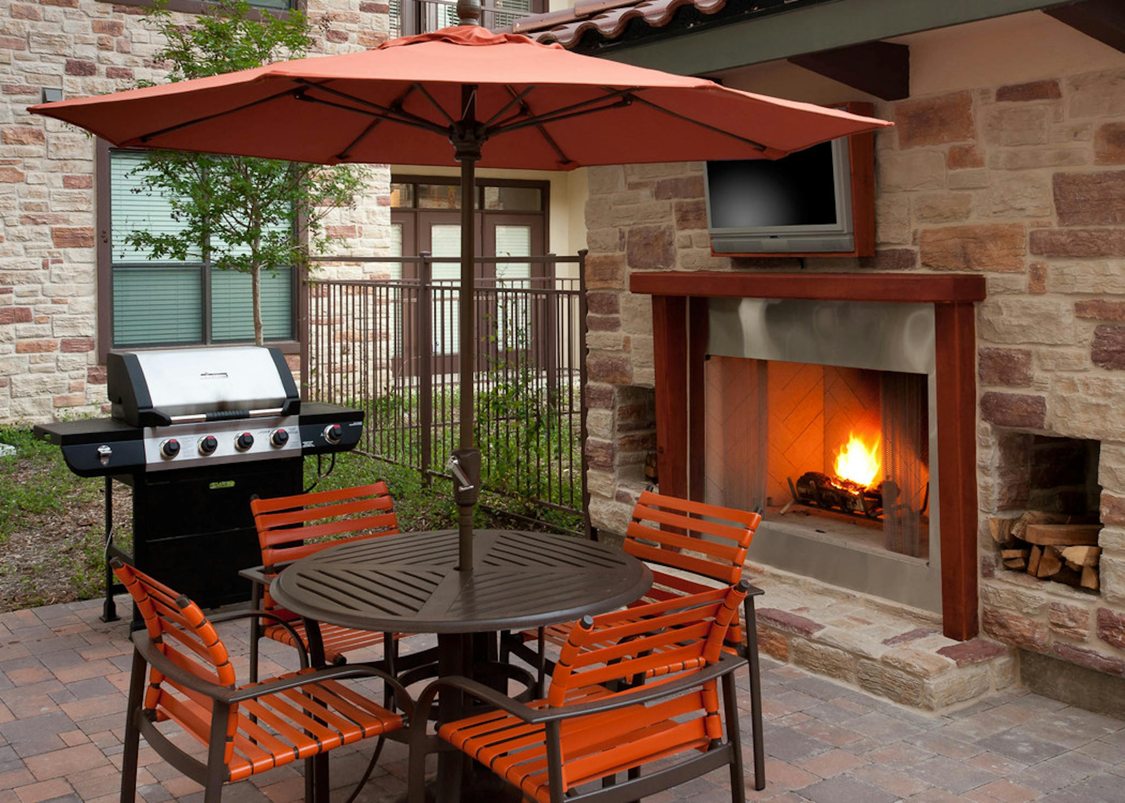 Daytime view of AMLI at Escena brick outdoor fireplace with brown table and four orange chairs and grill