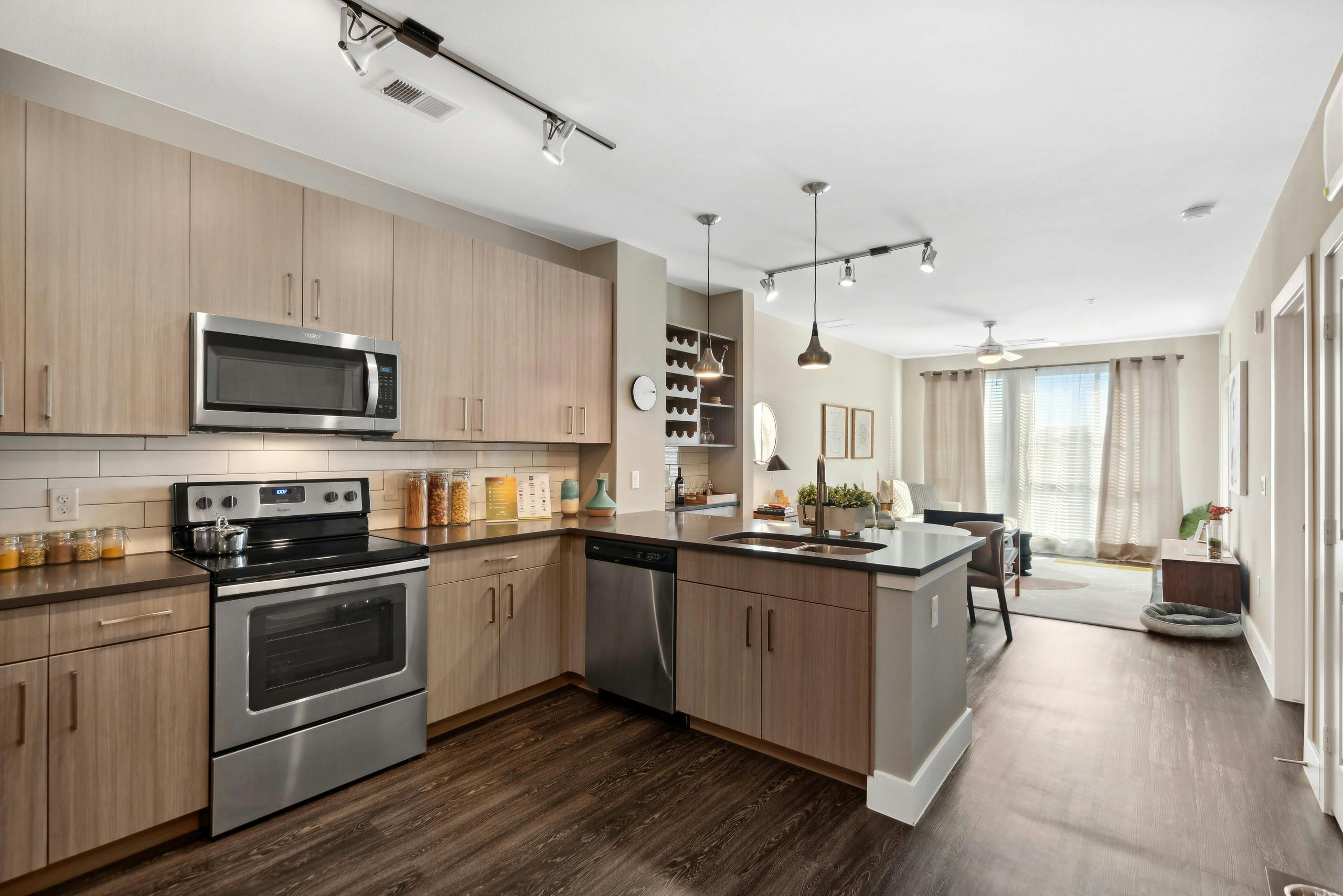 Interior view of a kitchen at AMLI Dry Creek apartments with tile back splash and several cabinets and view of living room