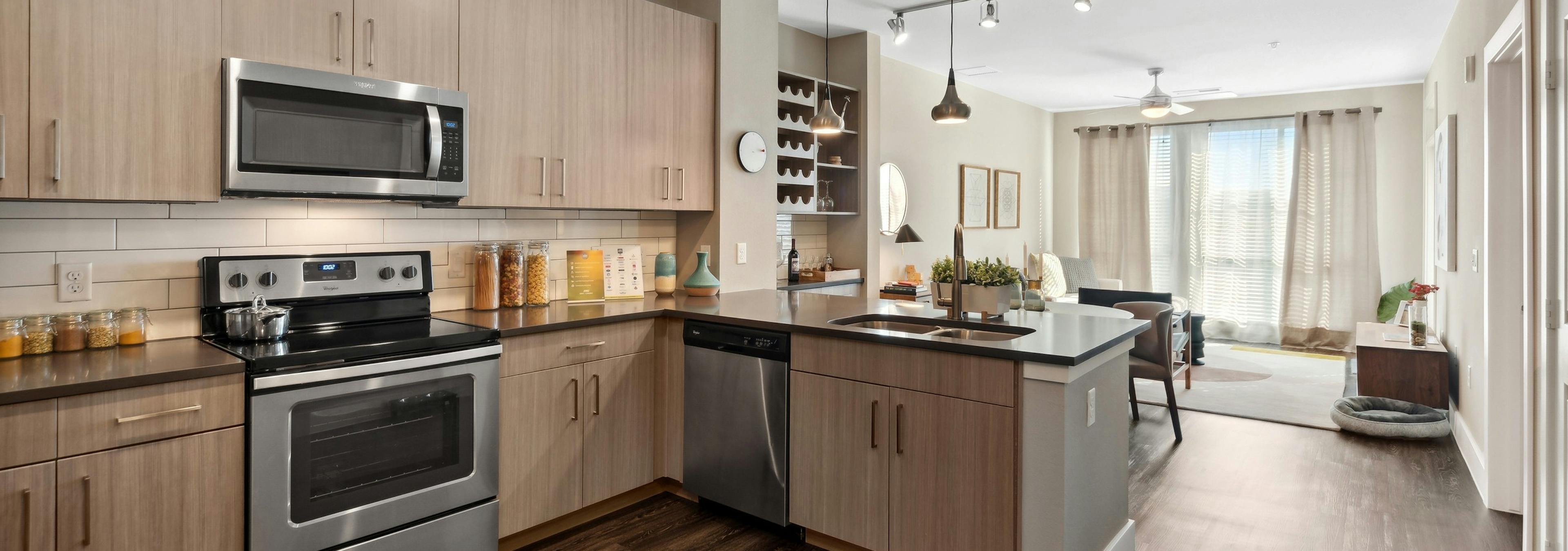 Interior view of a kitchen at AMLI Dry Creek apartments with tile back splash and several cabinets and view of living room