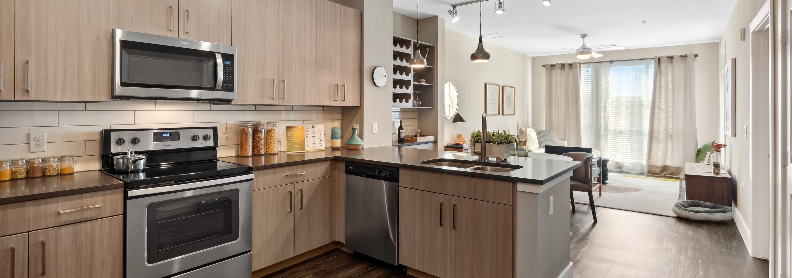 Interior view of a kitchen at AMLI Dry Creek apartments with tile back splash and several cabinets and view of living room