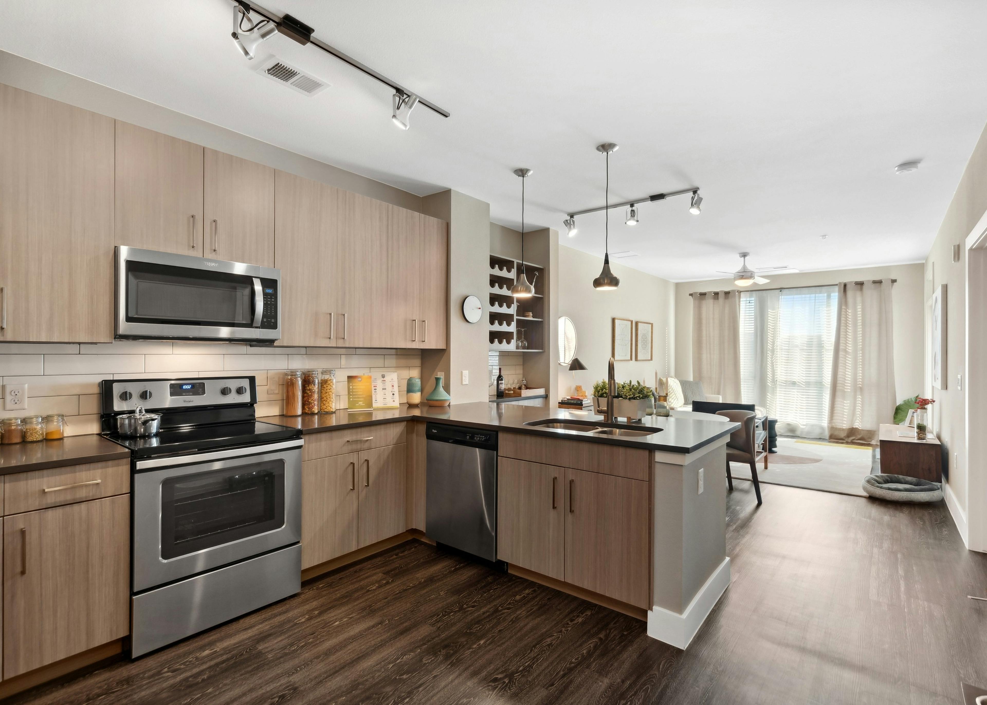 Interior view of a kitchen at AMLI Dry Creek apartments with tile back splash and several cabinets and view of living room