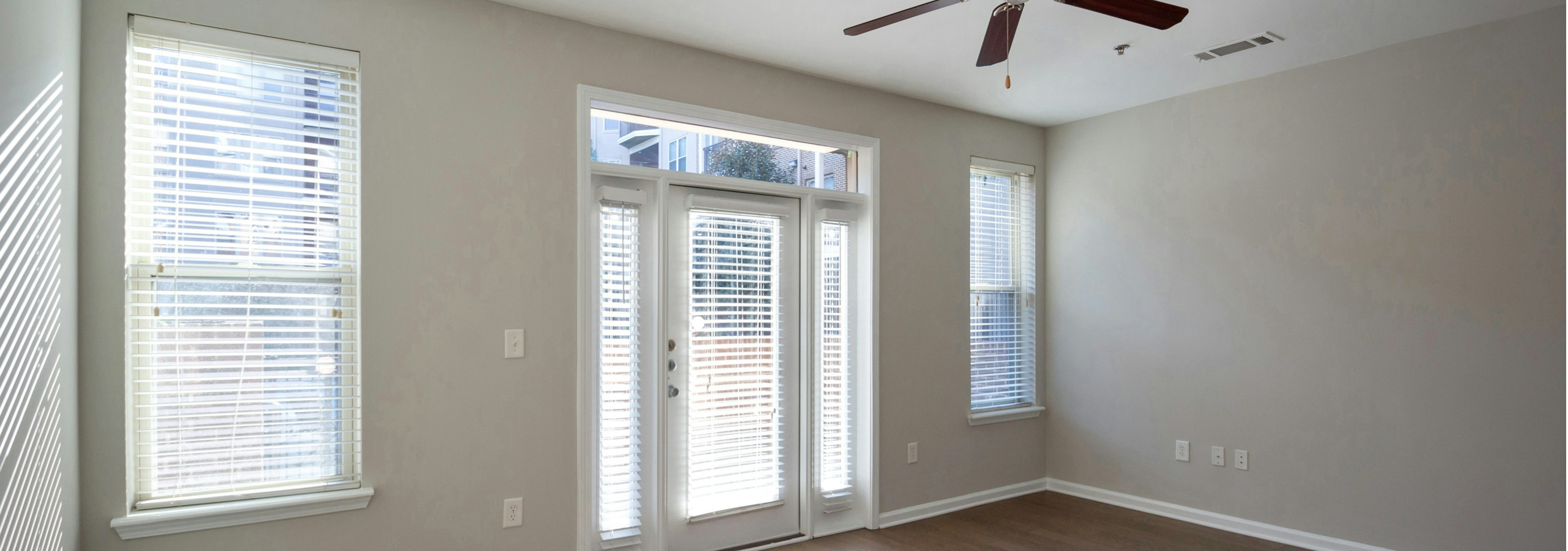 Interior of AMLI Lindbergh living room with light hardwood flooring and cream walls with a ceiling fan and bright windows