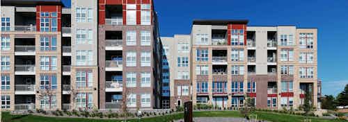 Exterior view of AMLI Dry Creek apartments showcasing several balconies and windows and green grass and trees and blue sky