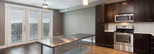 AMLI 5350 kitchen with dark wood cabinets and a white backsplash with lighter hardwood and floor to ceiling balcony doors