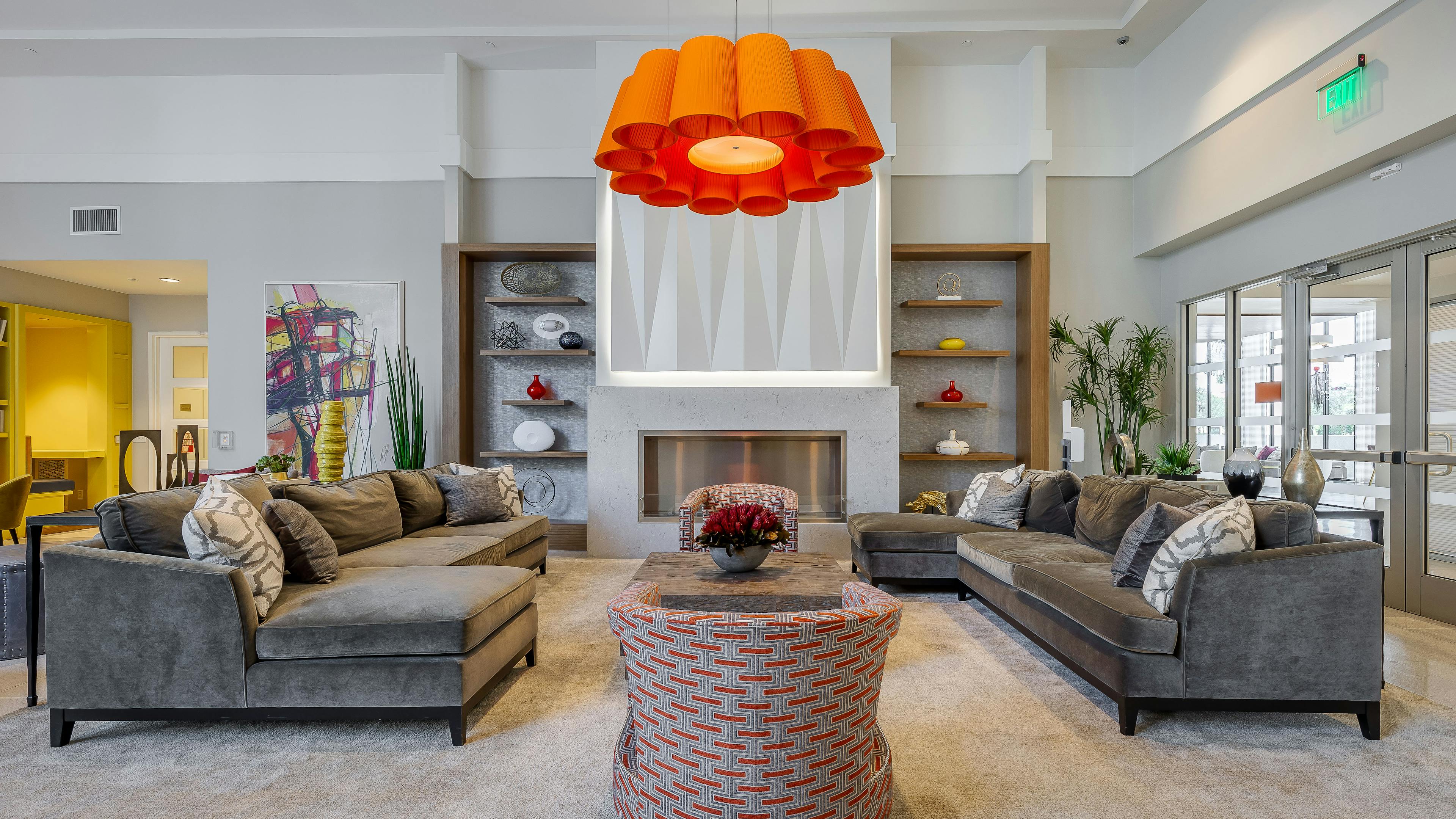 The resident lounge at AMLI 8800 apartments with gray sectionals and floral chandelier and a TV on the wall and a fireplace