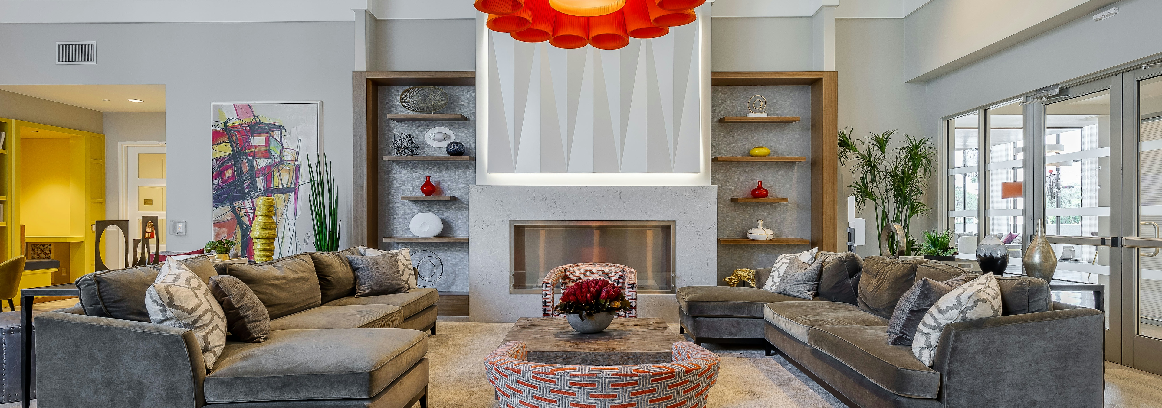 The resident lounge at AMLI 8800 apartments with gray sectionals and floral chandelier and a TV on the wall and a fireplace