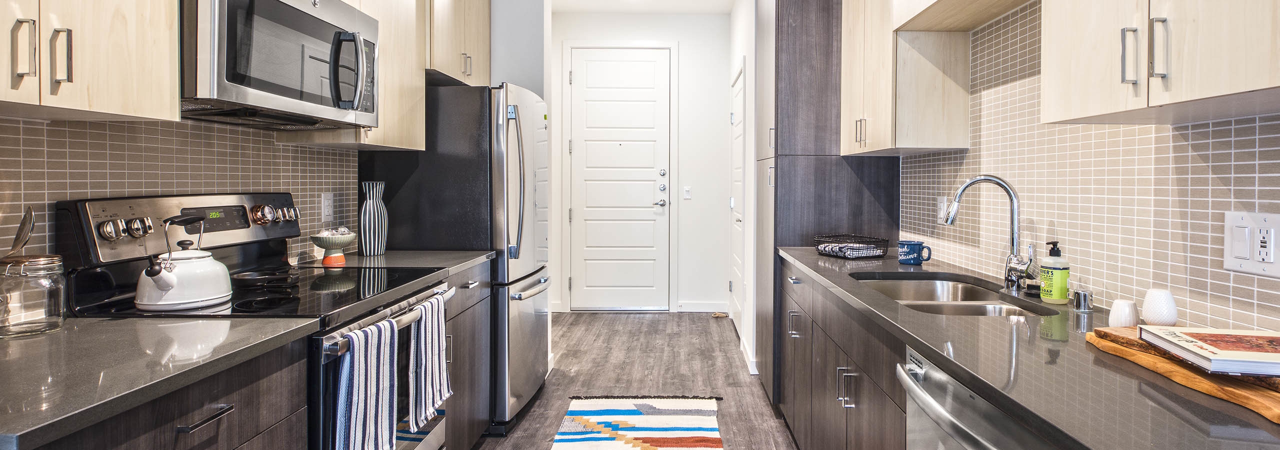 Interior view of an AMLI Wallingford apartment kitchen with two tone light and dark cabinets grey quartz counter tops and stainless steel appliances