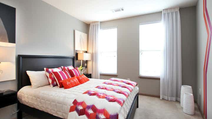 Interior of AMLI Lindbergh bedroom with tan walls and large windows with flowing curtains and burgundy decor accents