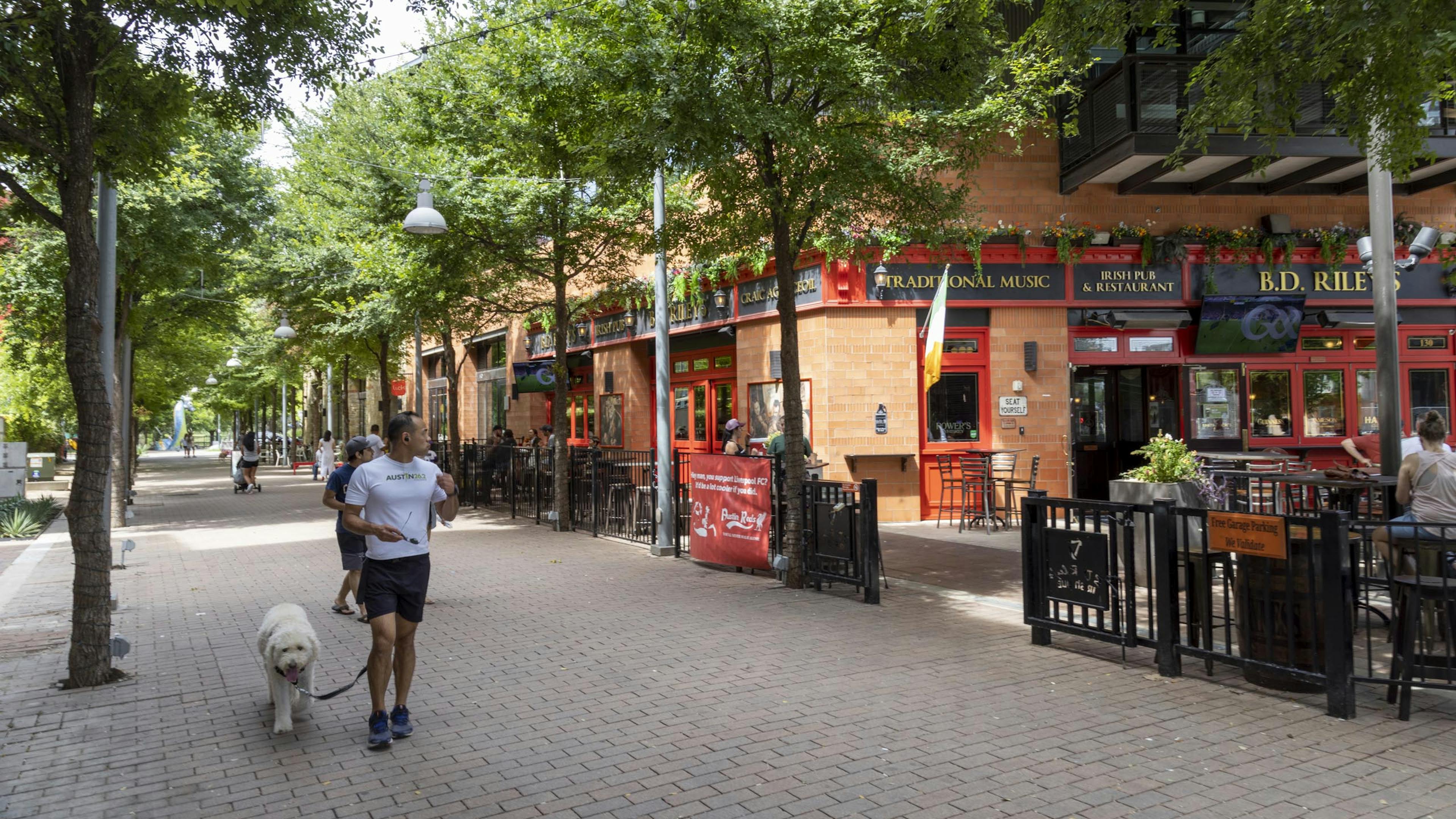 Retail district in Austin Mueller neighborhood featuring an Irish restaurant with outdoor seating and a passerby with his dog