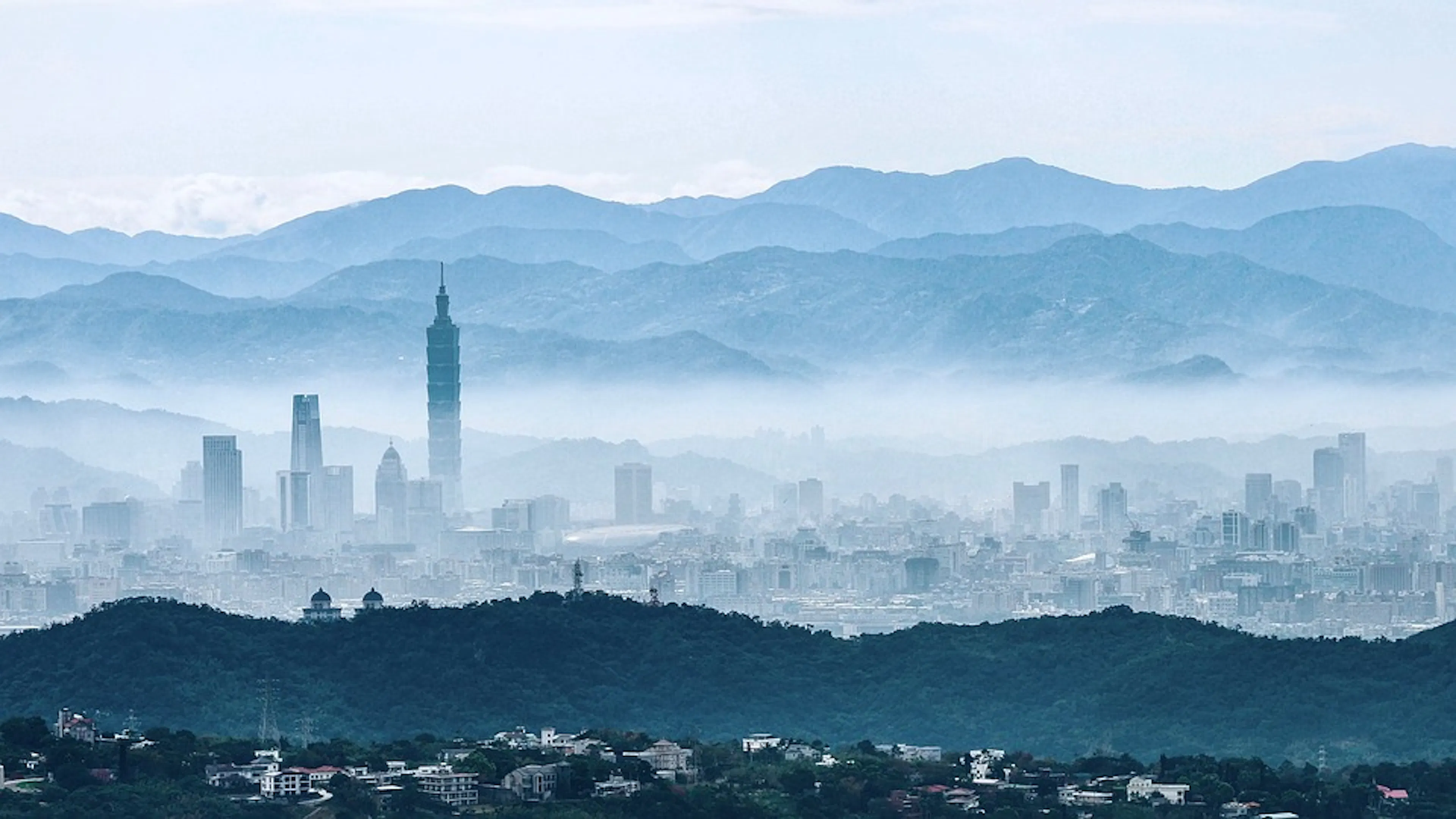 The city of Taipei peeking through a layer of fog with mountains in the background