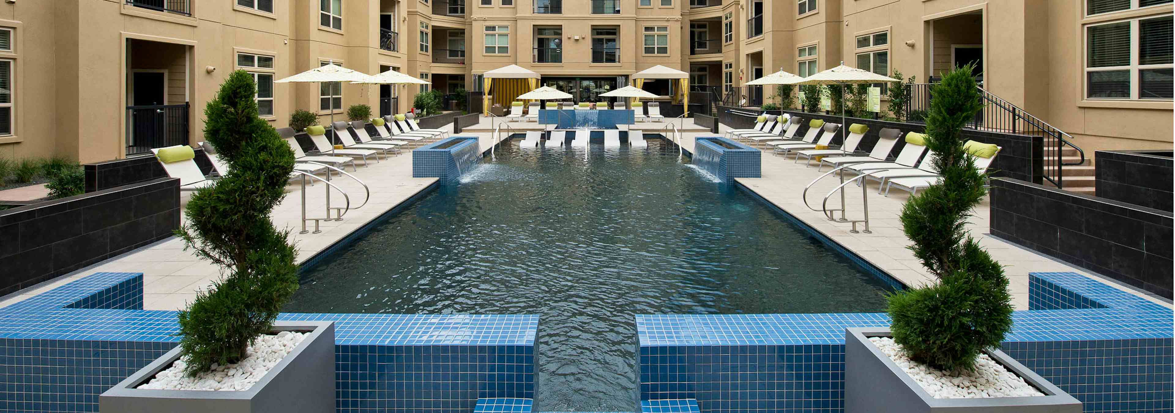 Daytime view of AMLI RidgeGate pool with blue tile cascading waterfalls onto pool and Jacuzzi sides and water ledge loungers