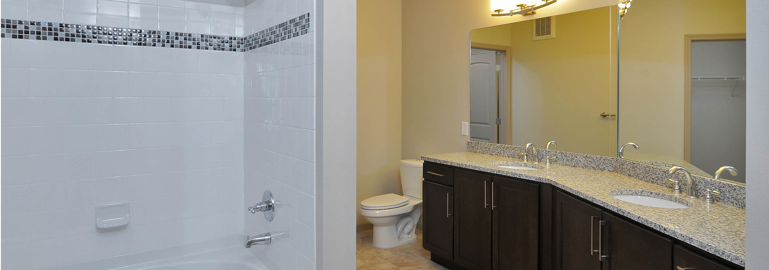 AMLI North Point bathroom with white tiled bathtub and long double vanity sink with dark cabinets and granite countertops