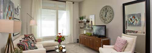 Interior view of living room at AMLI 5350 with white seating and carpeted flooring with a large window and light walls