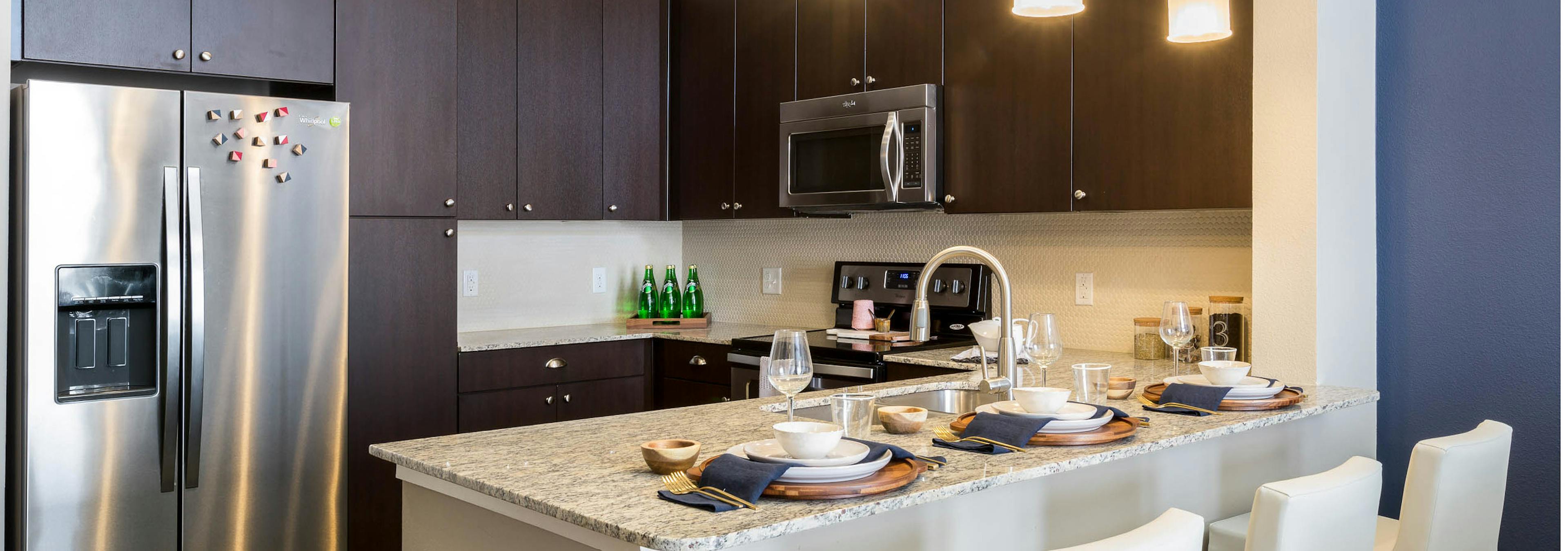 Kitchen at AMLI on Riverside with dark wood cabinets and granite countertops with creme backplash and barstools at counter