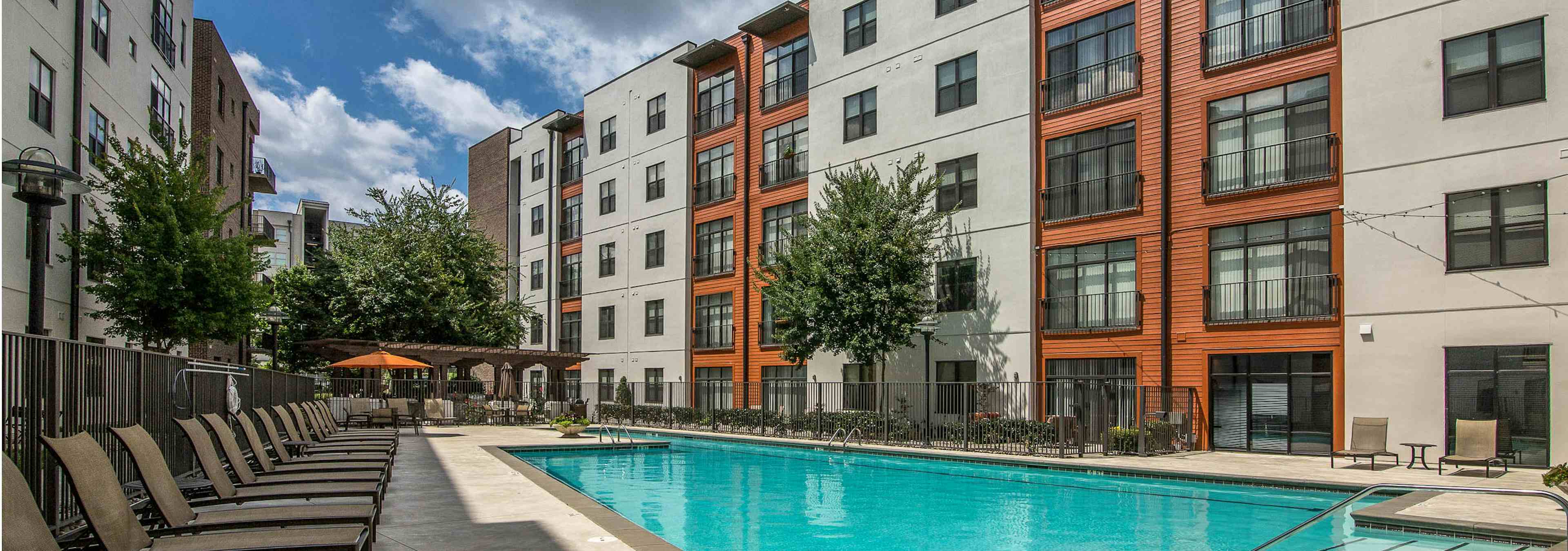 Sunny daytime view of a swimming pool surrounded by tan lounge chairs on both sides of the water at AMLI 4th Ward