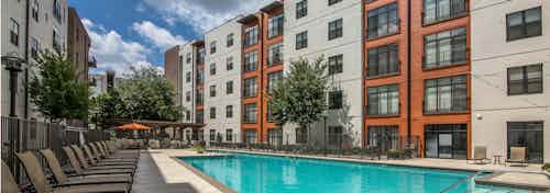 Sunny daytime view of a swimming pool surrounded by tan lounge chairs on both sides of the water at AMLI 4th Ward