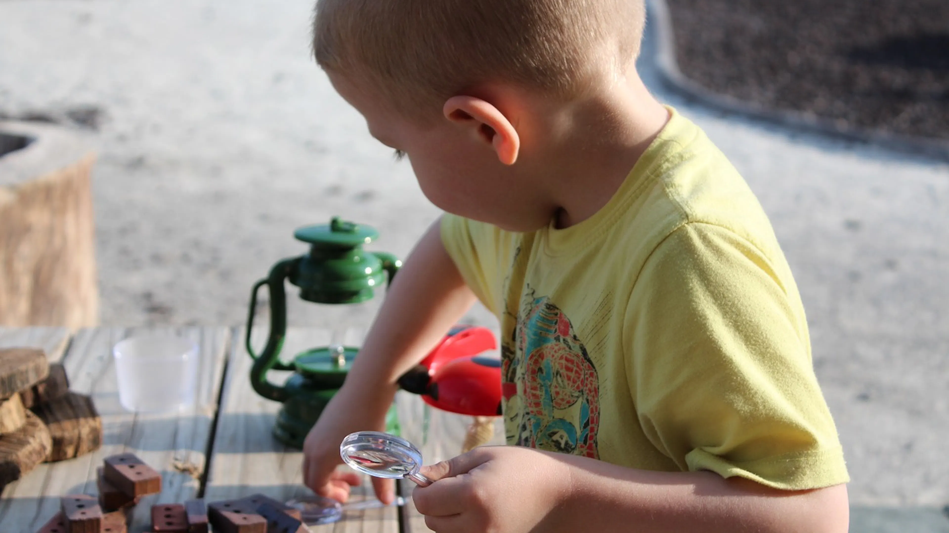A small boy playing with a toy set of bricks and a small magnifying glass outside on a wooden bench