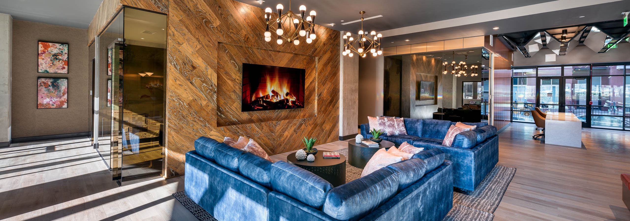 AMLI Art District leasing office with blue plush couches and large rugs and a TV and two chandeliers overhead