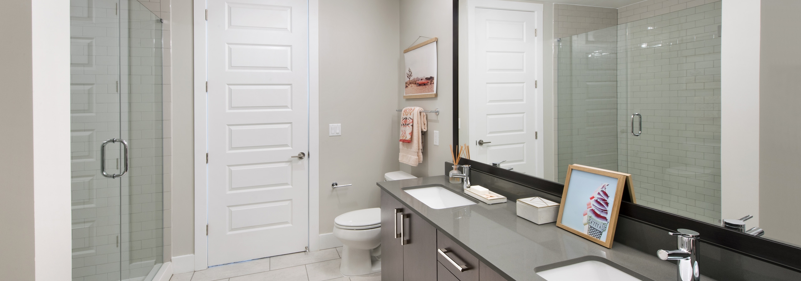 AMLI Lenox apartment bathroom with glass shower and double vanity and dark cabinets and quartz countertop with big mirror