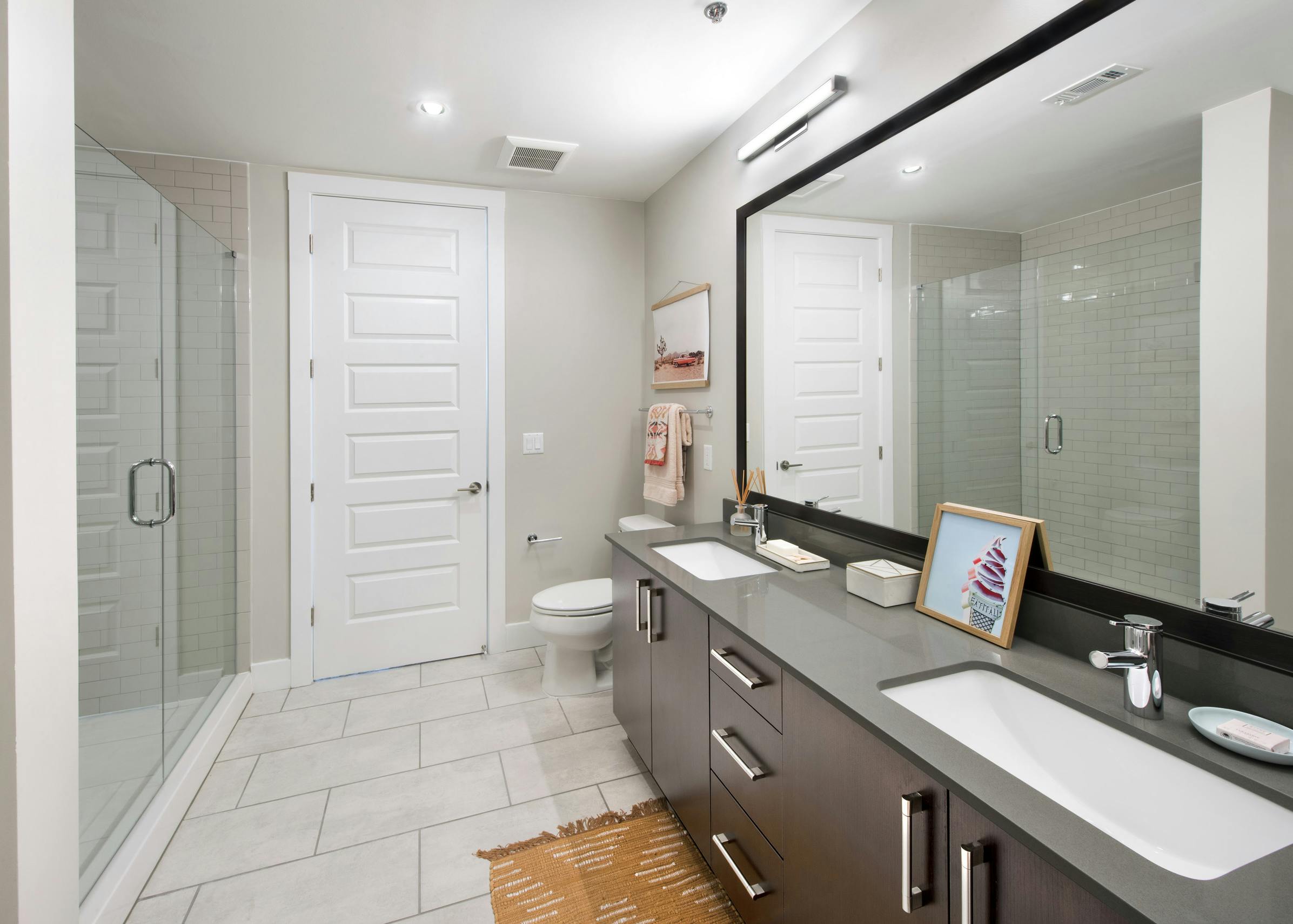 AMLI Lenox apartment bathroom with glass shower and double vanity and dark cabinets and quartz countertop with big mirror