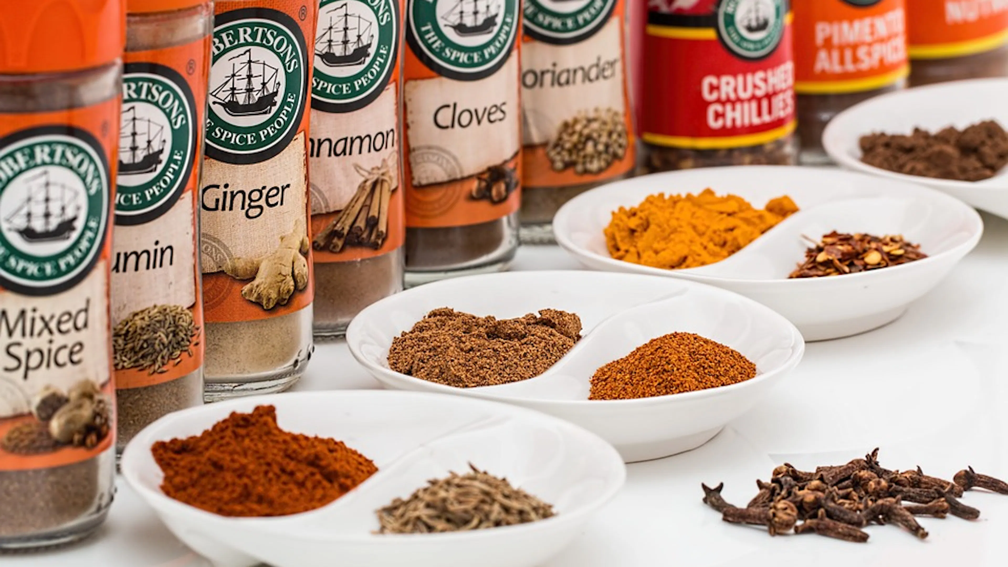A row of glass spice jars with little piles of spices next to them in all different colors