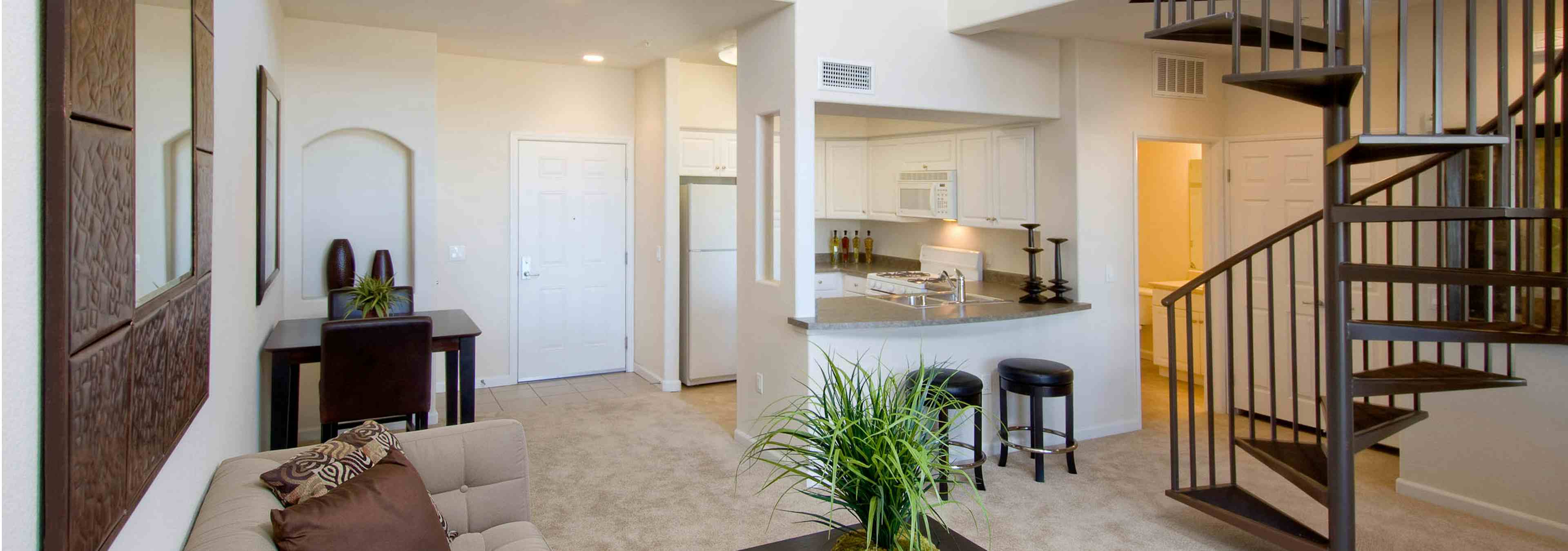 Interior of AMLI Warner Center apartment kitchen and living room with spiral staircase, carpet and peek into lit bathroom